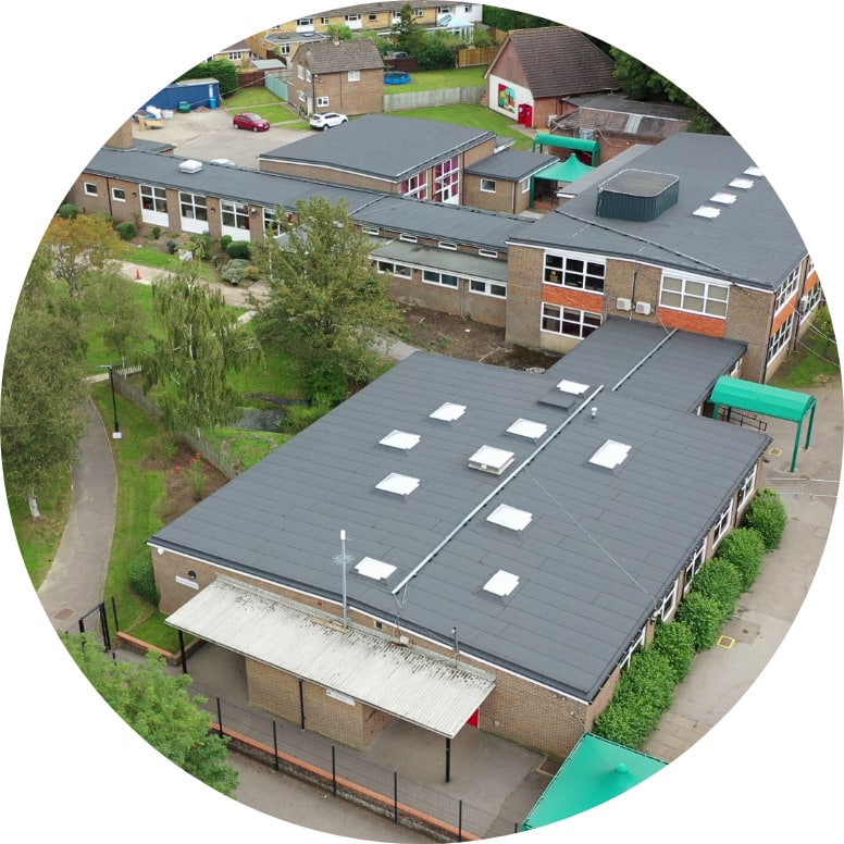 Aerial view of a school complex with multiple flat roofed buildings arranged around a courtyard, featuring grey roofs and red brick walls