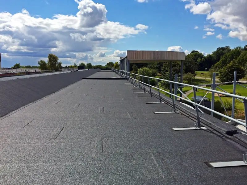 Flat roof membrane installation with metal railing and industrial building structure