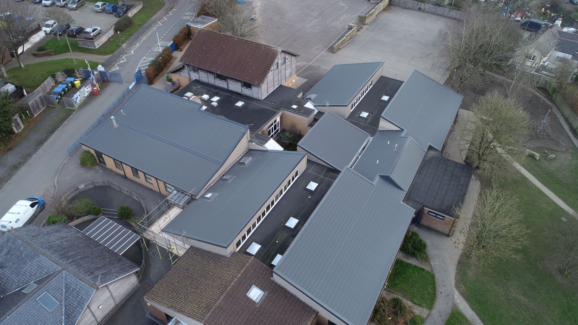 Aerial view of several connected low rise buildings with pitched roofs arranged around a courtyard with grass and trees