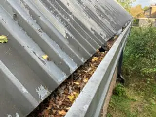 blocked gutter with leaves and corroded metal roofing profile
