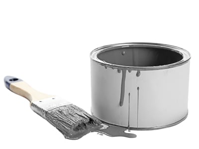 Open metal paint can with grey paint dripping down the side and a paintbrush resting next to it on a white background