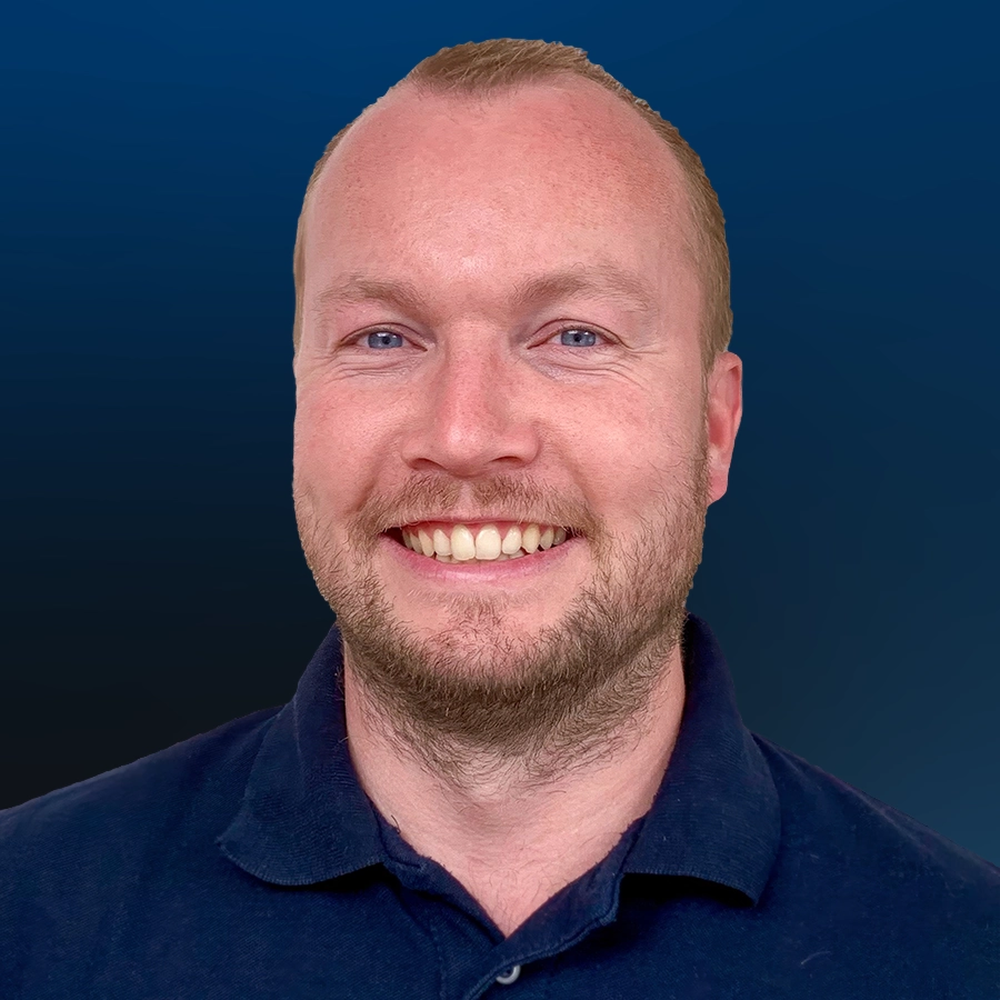 Smiling man with red hair and beard wearing dark blue polo shirt