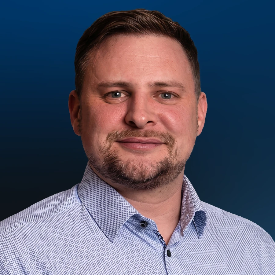 Professional headshot of man with beard wearing light blue button-up shirt