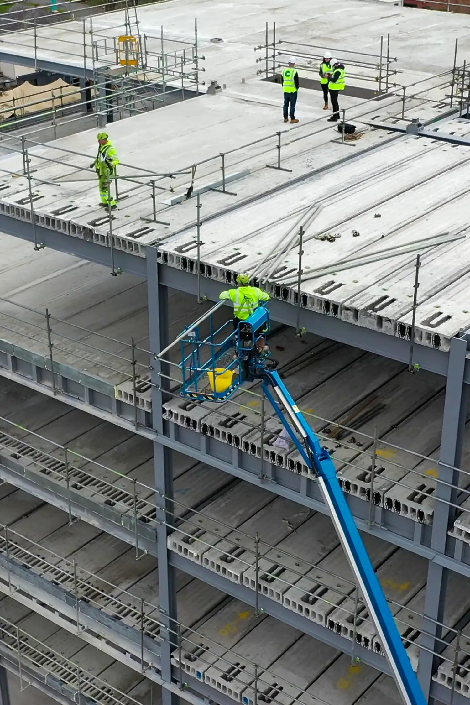 Construction workers in high-visibility gear on multi-story building framework with blue lift platform
