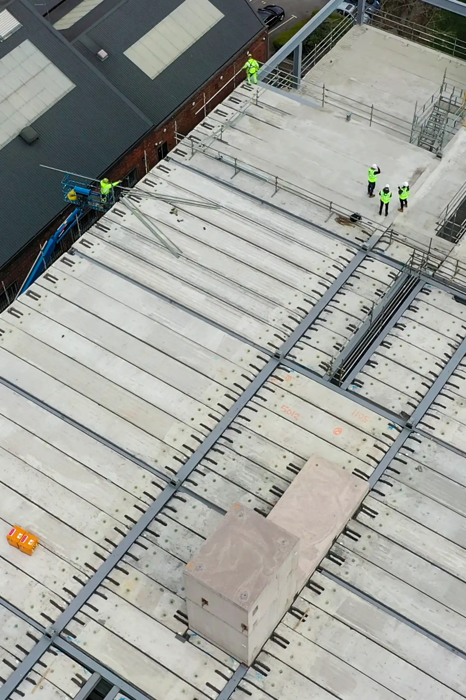 Aerial view of construction workers on concrete roof deck with steel framework and equipment.