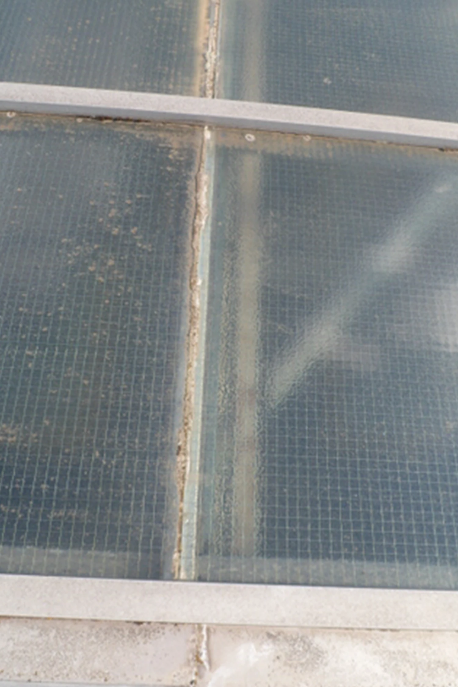 Dirty window screen with white frame and metal muntins showing dust accumulation