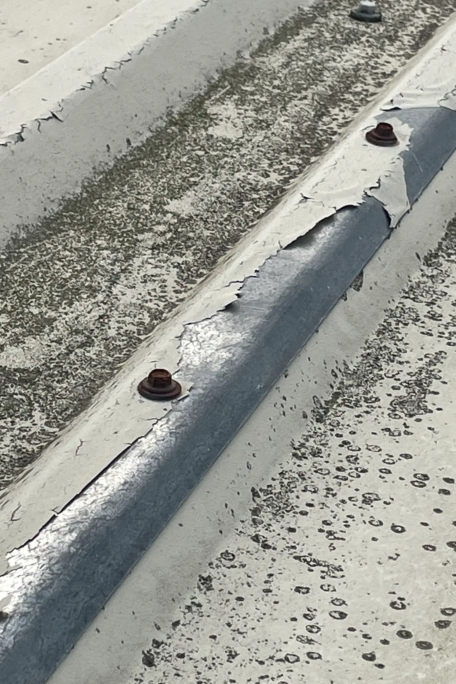 Damaged flat roof membrane with exposed metal pipe and fasteners showing deterioration
