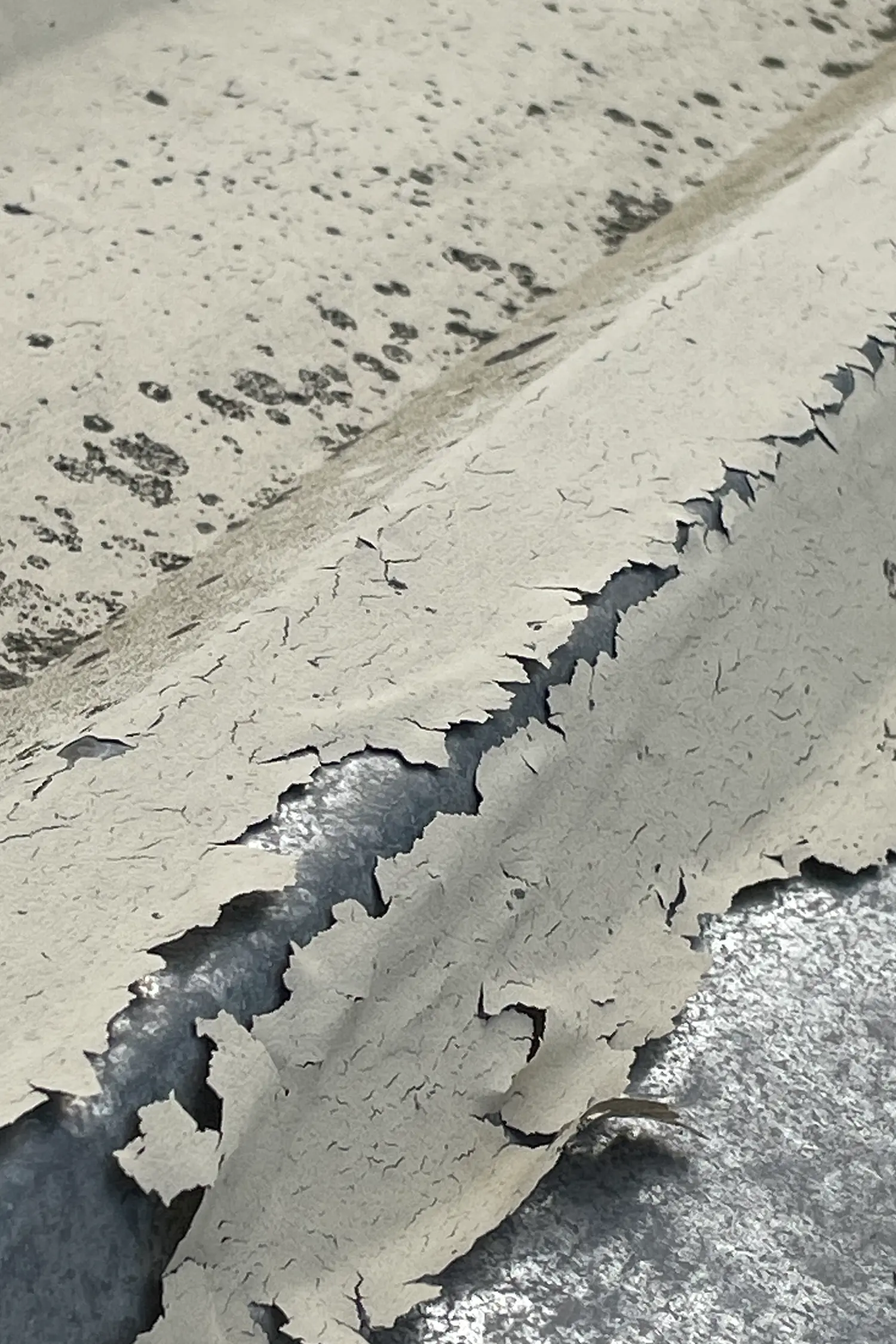Aerial view of cracked concrete surface with dark crevices and debris scattered across pavement.