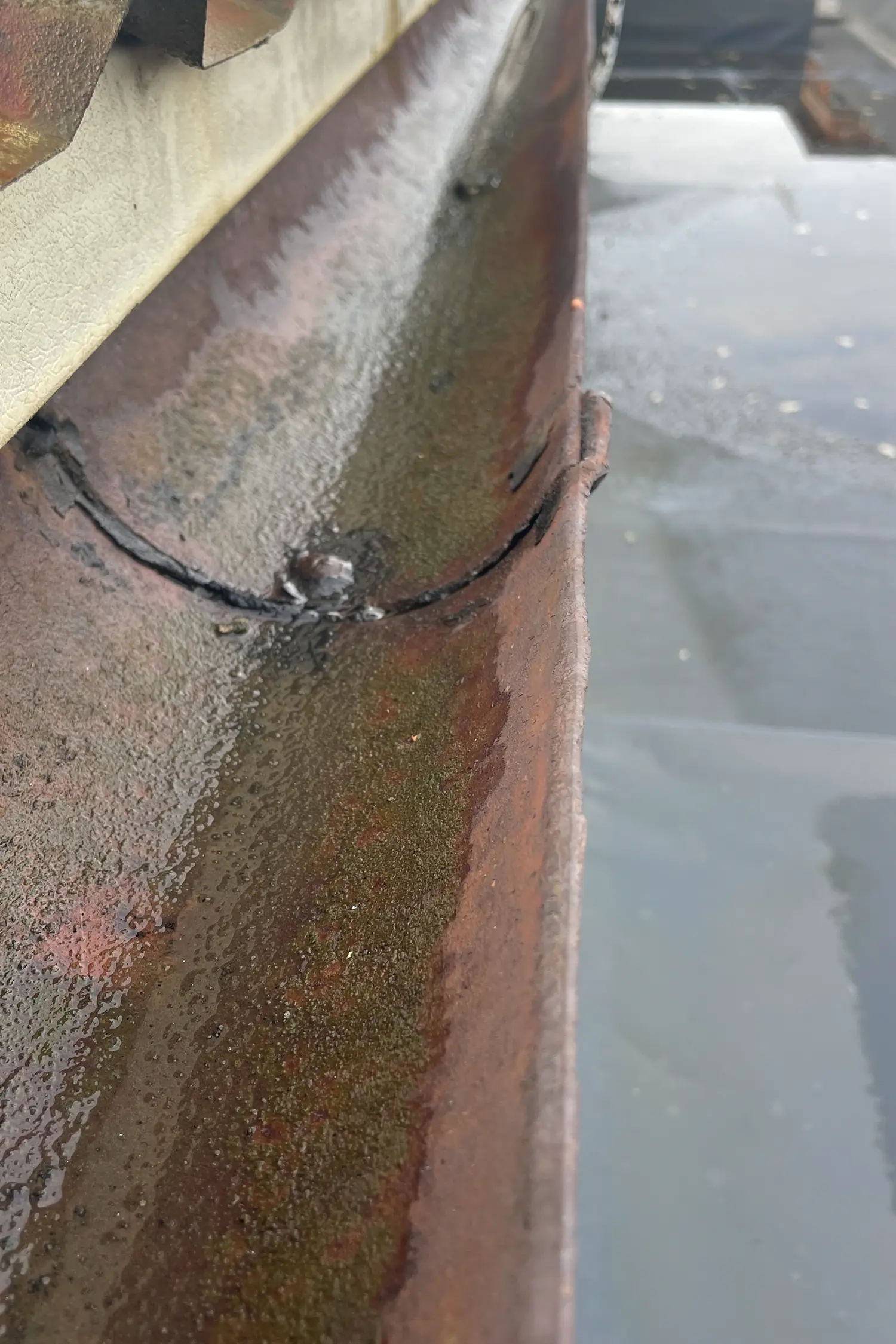 Rusted metal roof edge with algae growth and water droplets