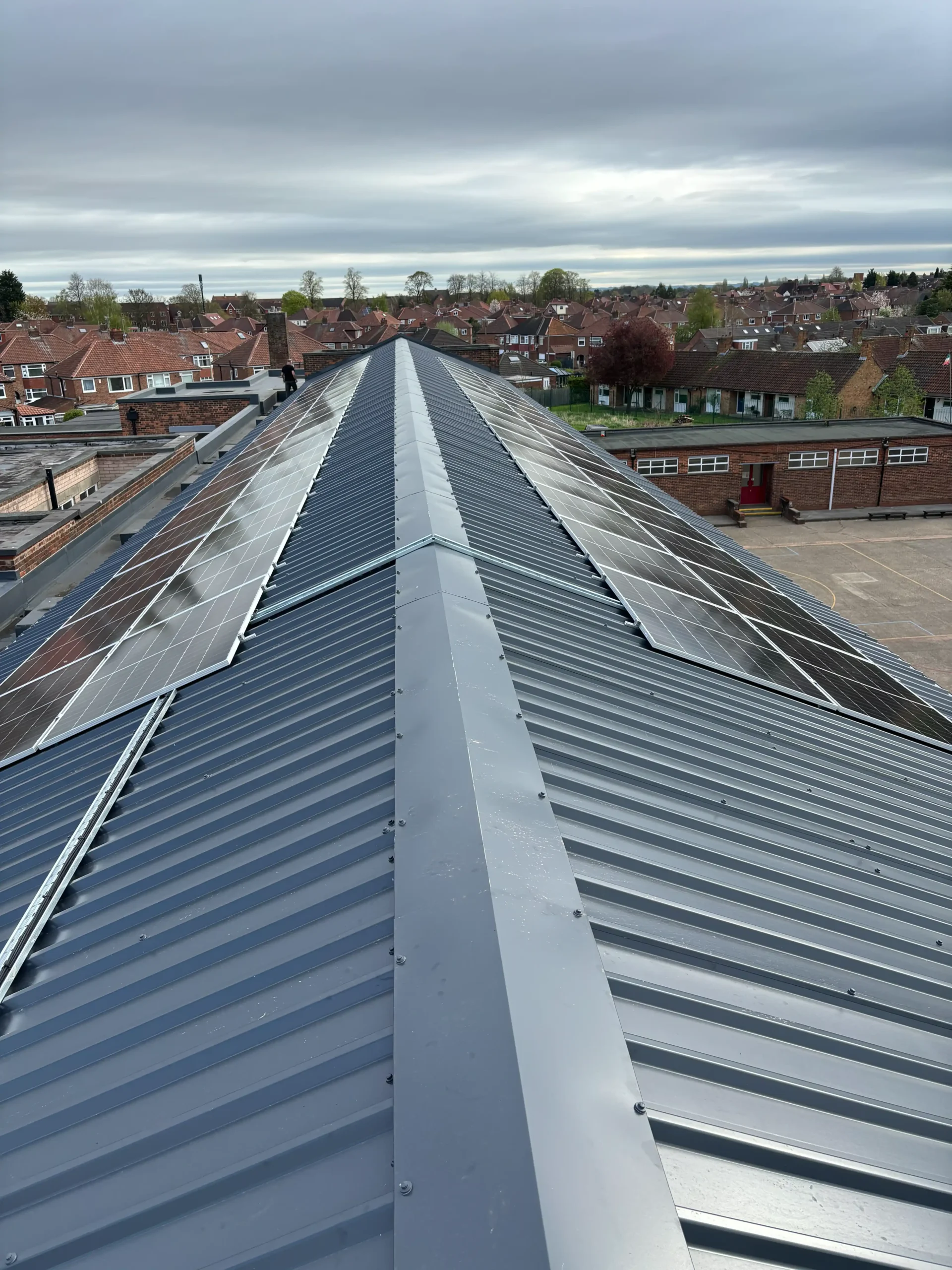 Aerial view of solar panels installed on school building roof with residential neighborhood beyond