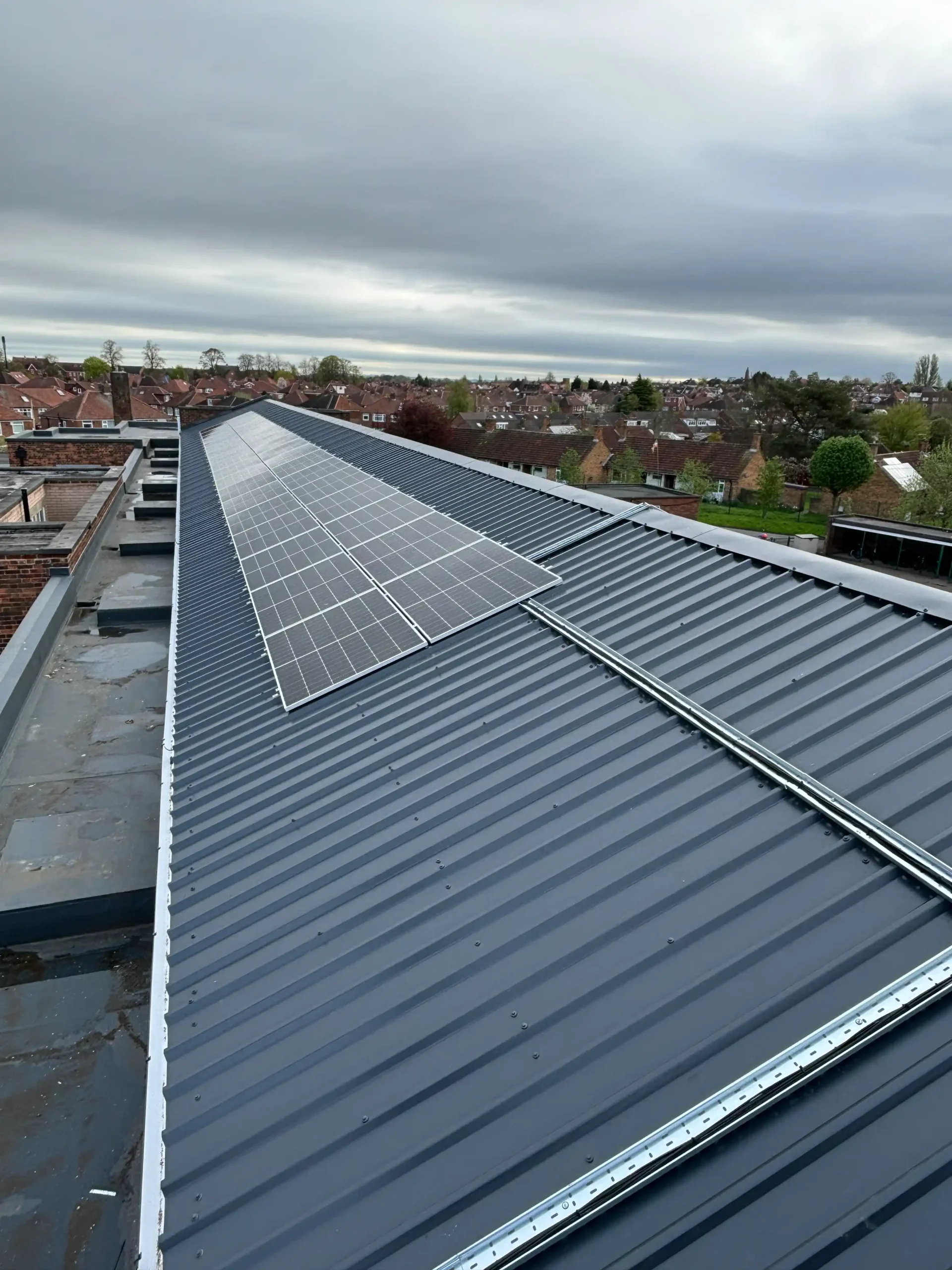 Solar panel array installed on corrugated metal roof overlooking suburban residential neighborhood