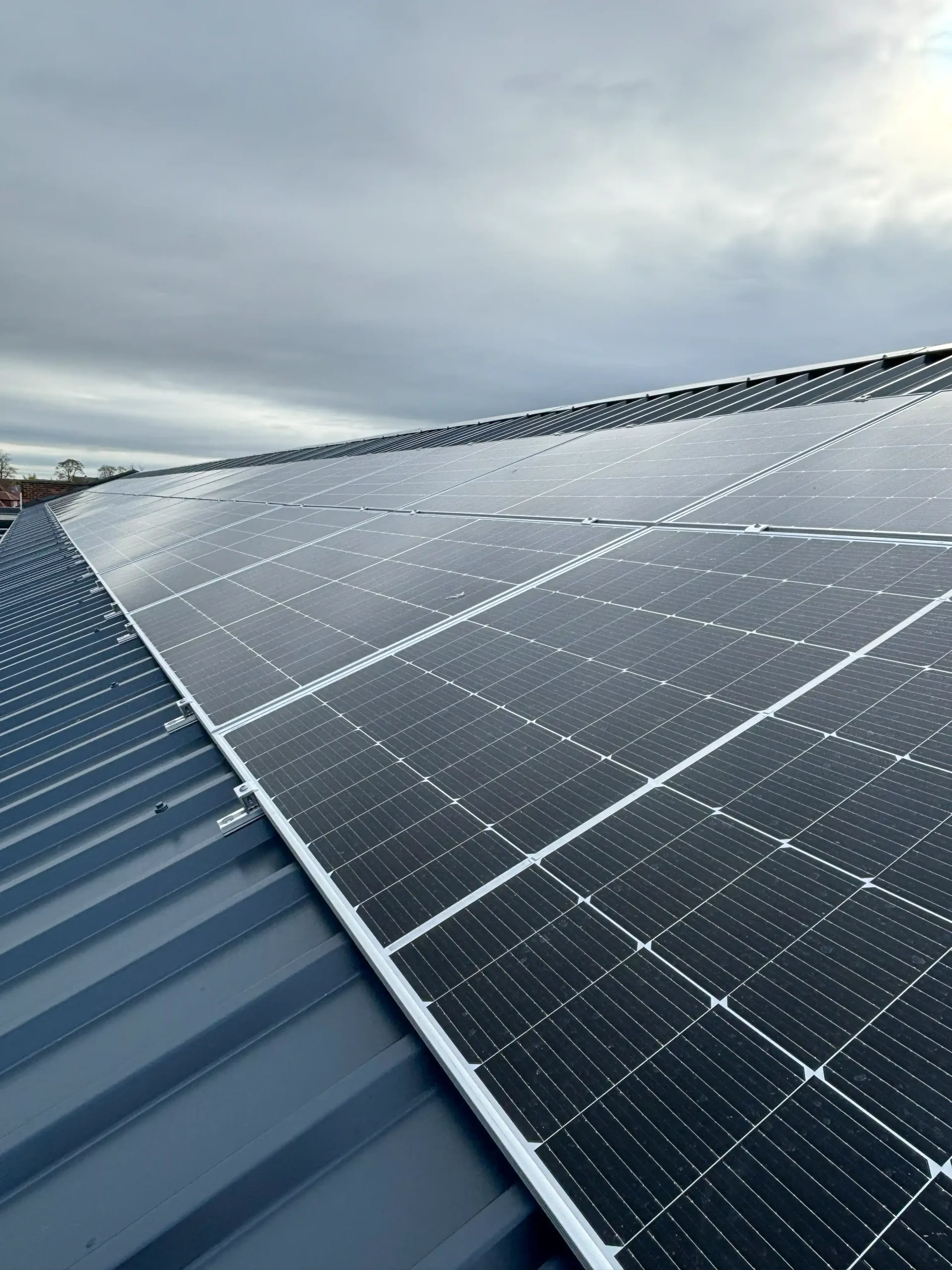 Solar panels installed on industrial metal roof under cloudy sky