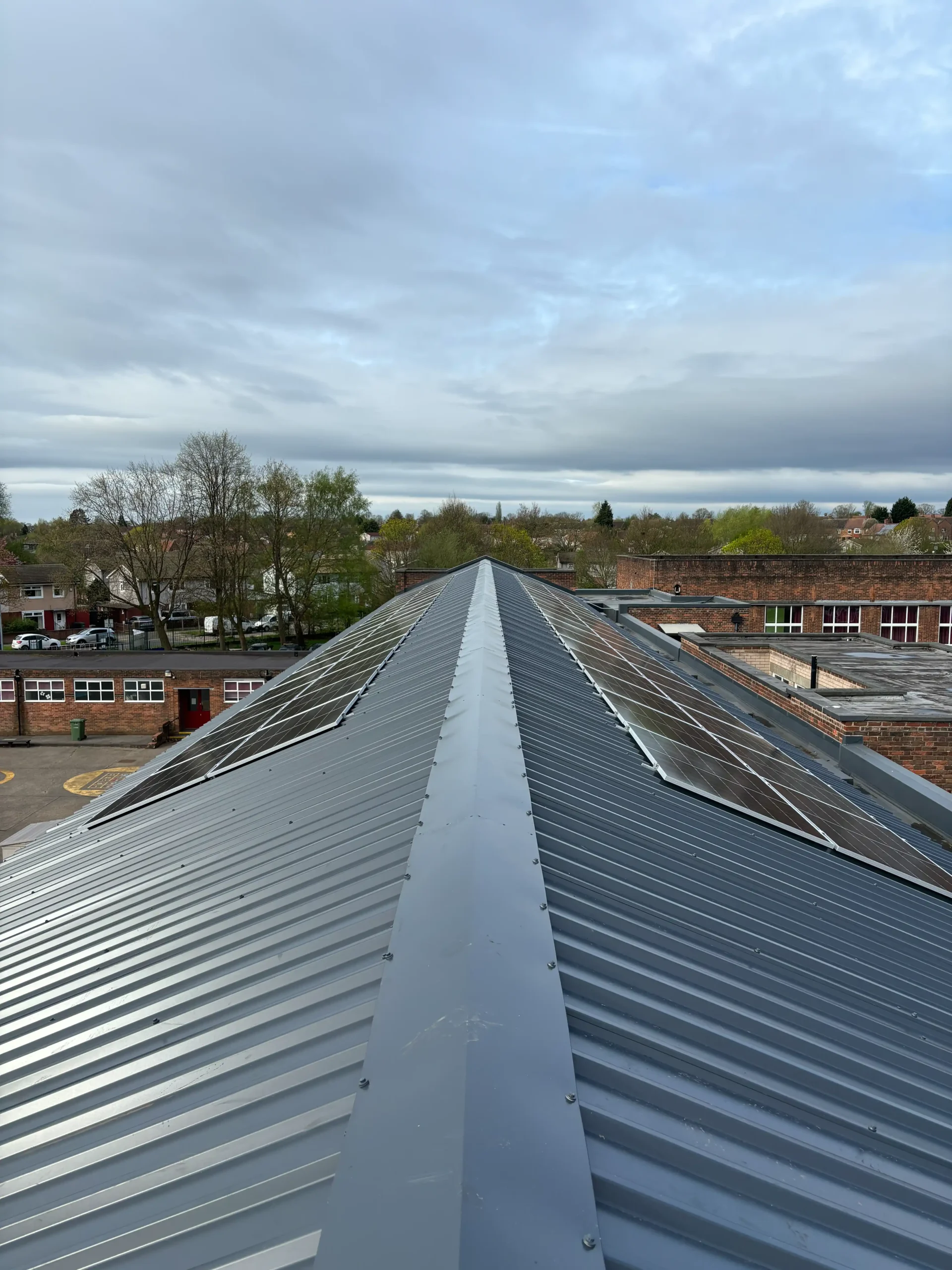 Metal roof ridge with white capping running toward suburban residential landscape