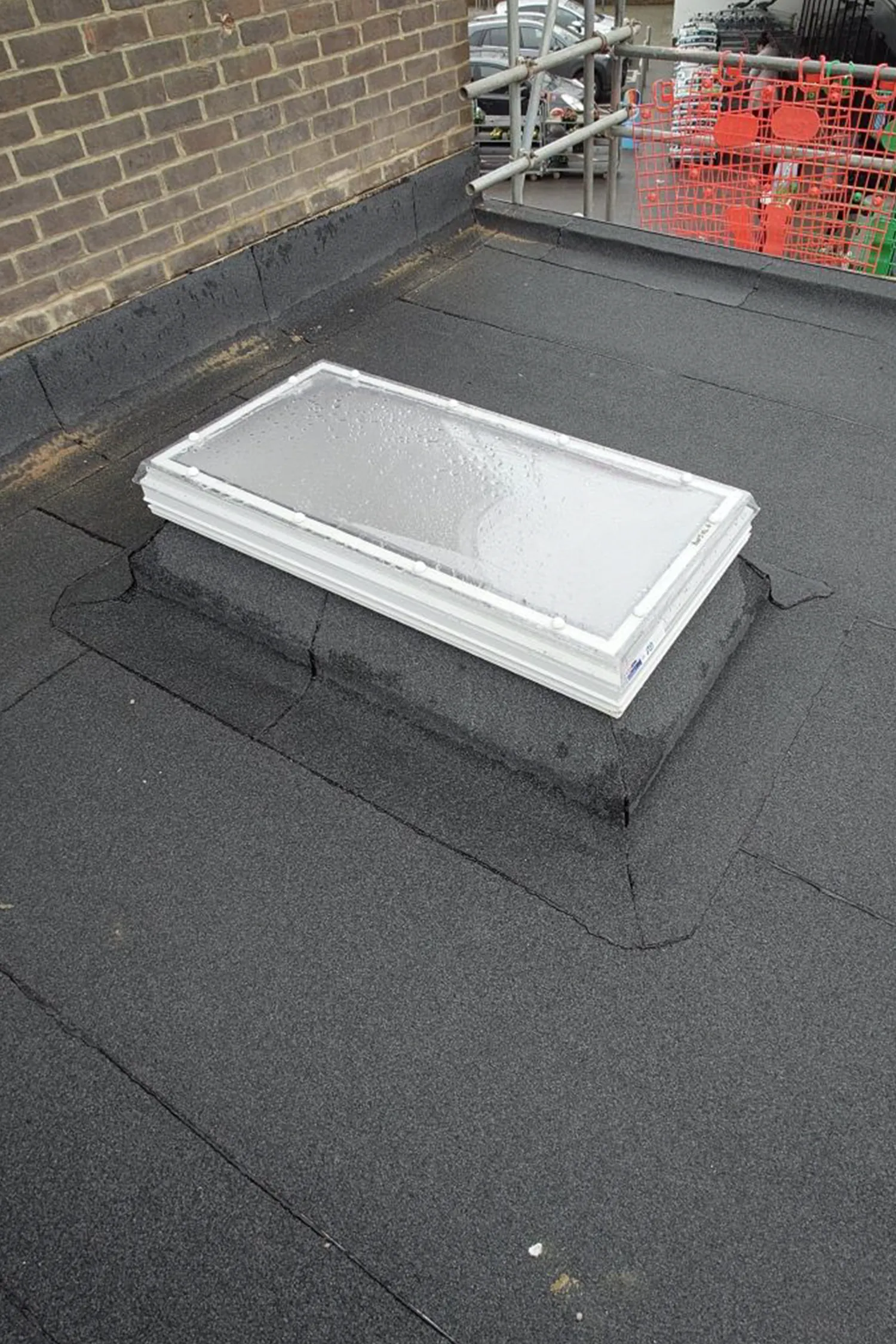 White skylight installed on dark flat roof with brick wall backdrop