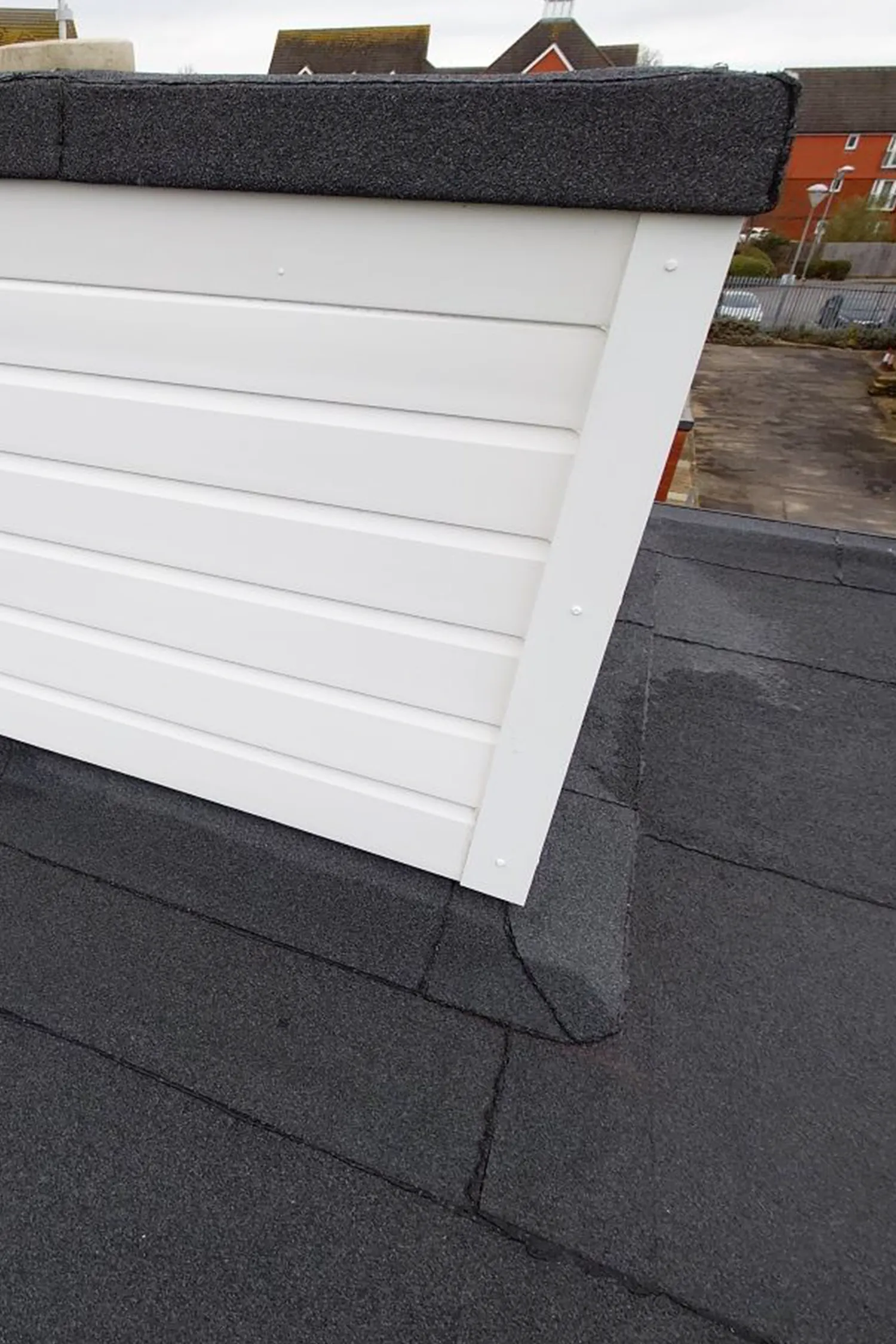 Roof installation showing white fascia board and dark asphalt shingles detail.