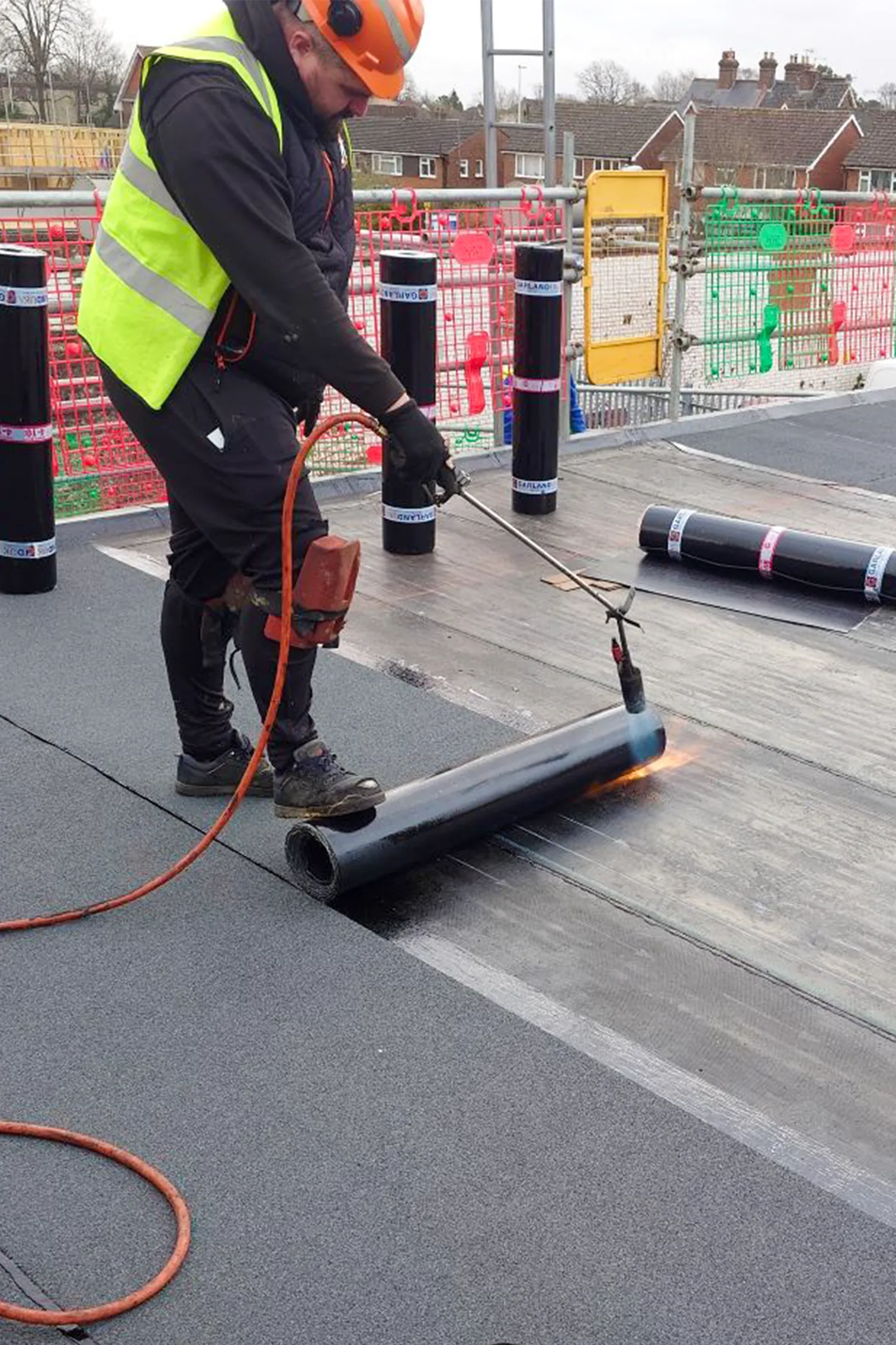 Worker using heat gun to install roofing membrane on flat roof surface