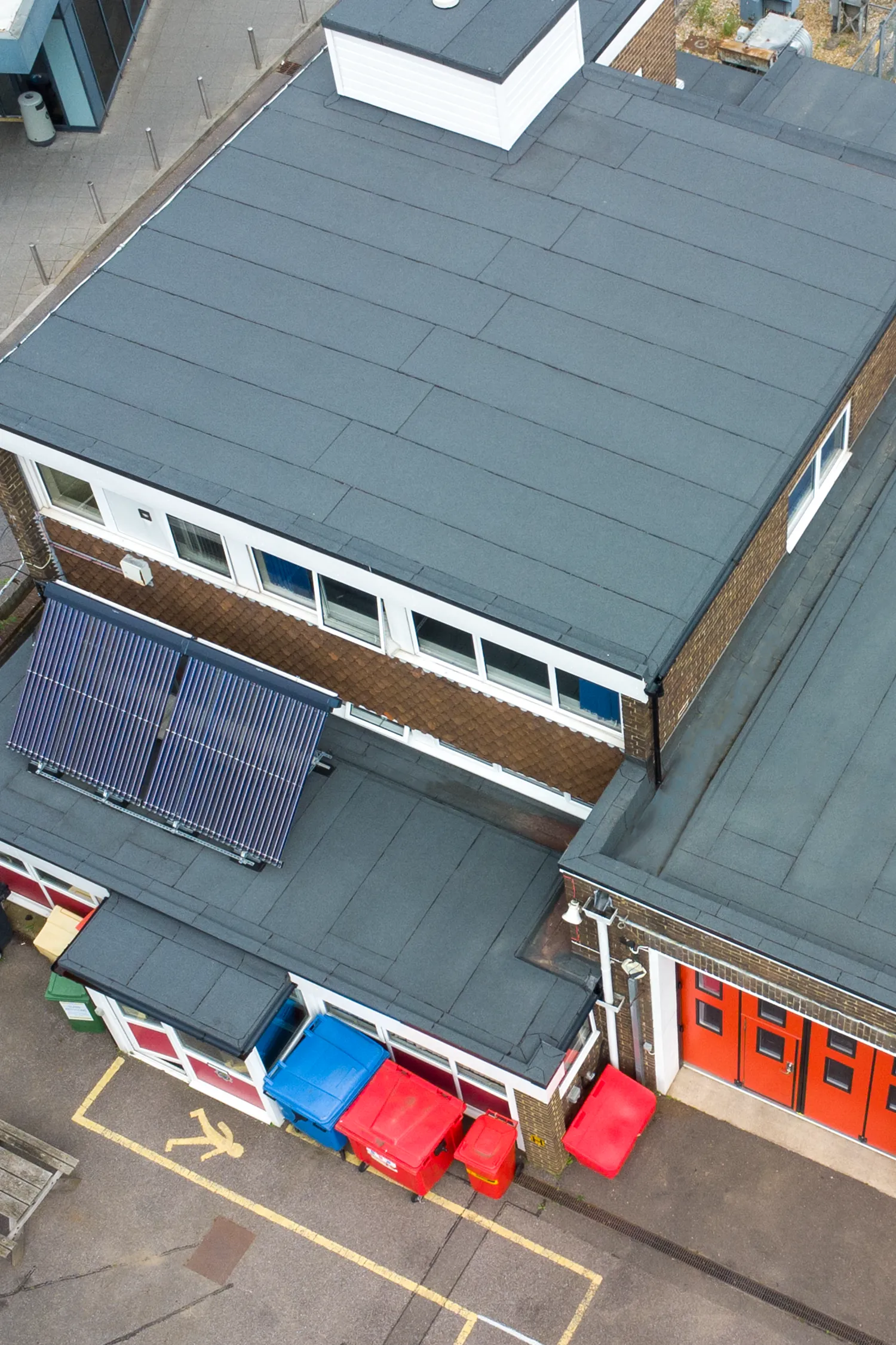 Aerial view of fire station with solar panels on roof and red bins below