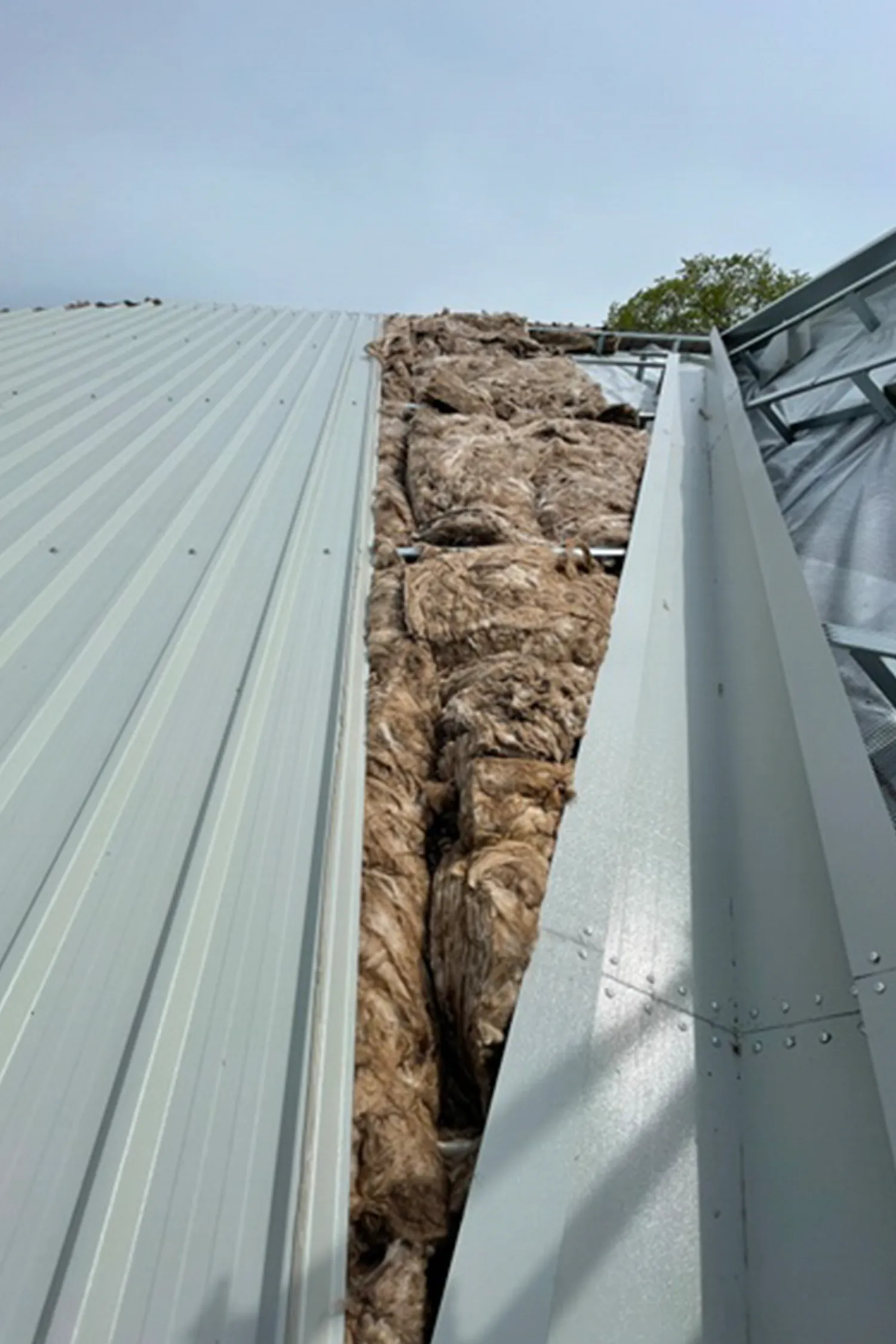 Metal building gutters filled with insulation material between corrugated panels