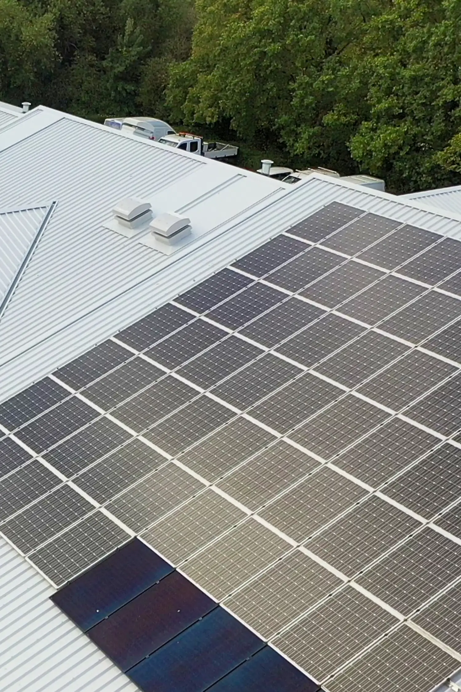 Aerial view of solar panels installed on commercial metal roof with trees