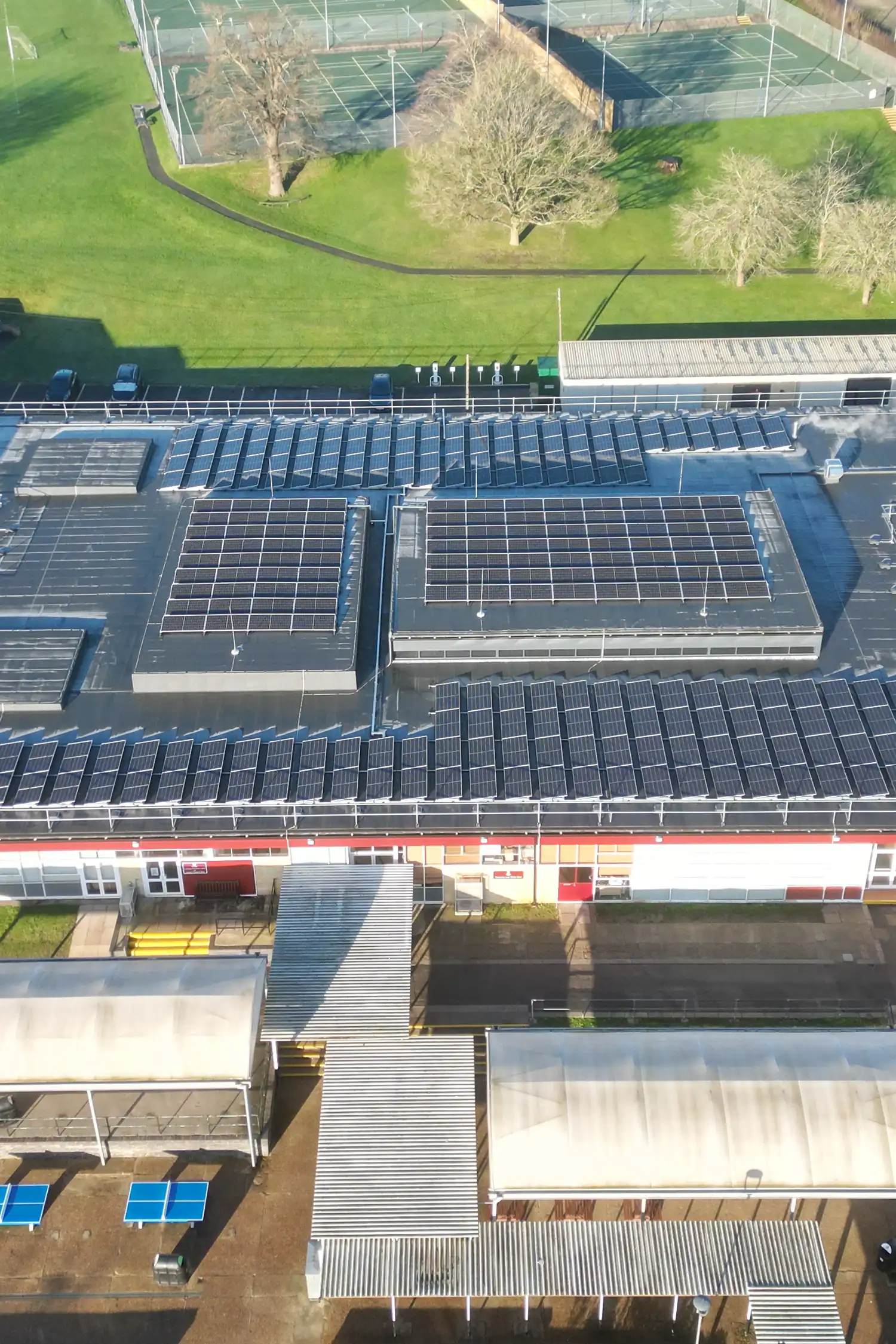 Aerial view of school sports facility with extensive rooftop solar panels installation