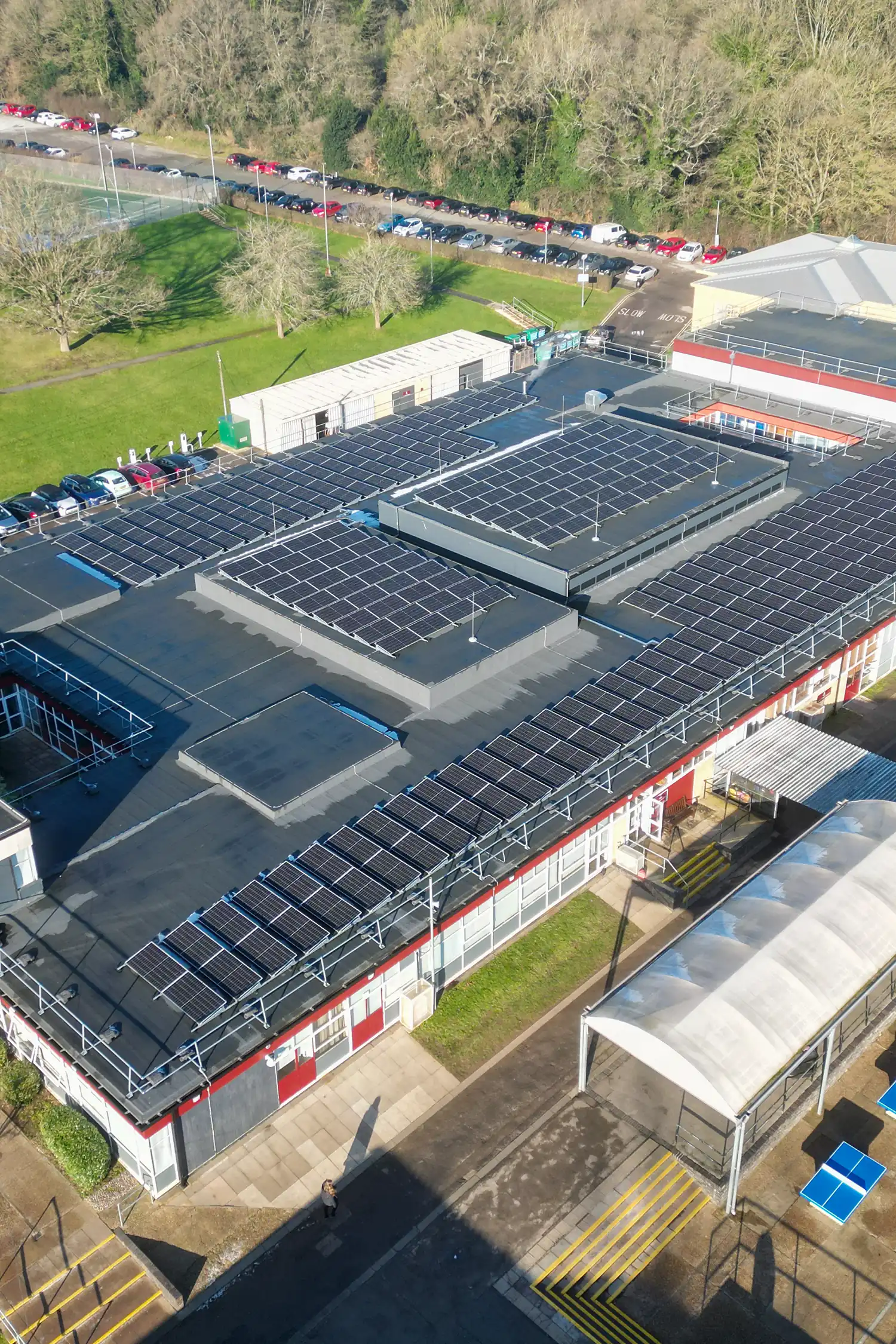 Aerial view of sports facility with solar panels on multiple courts and parking area.