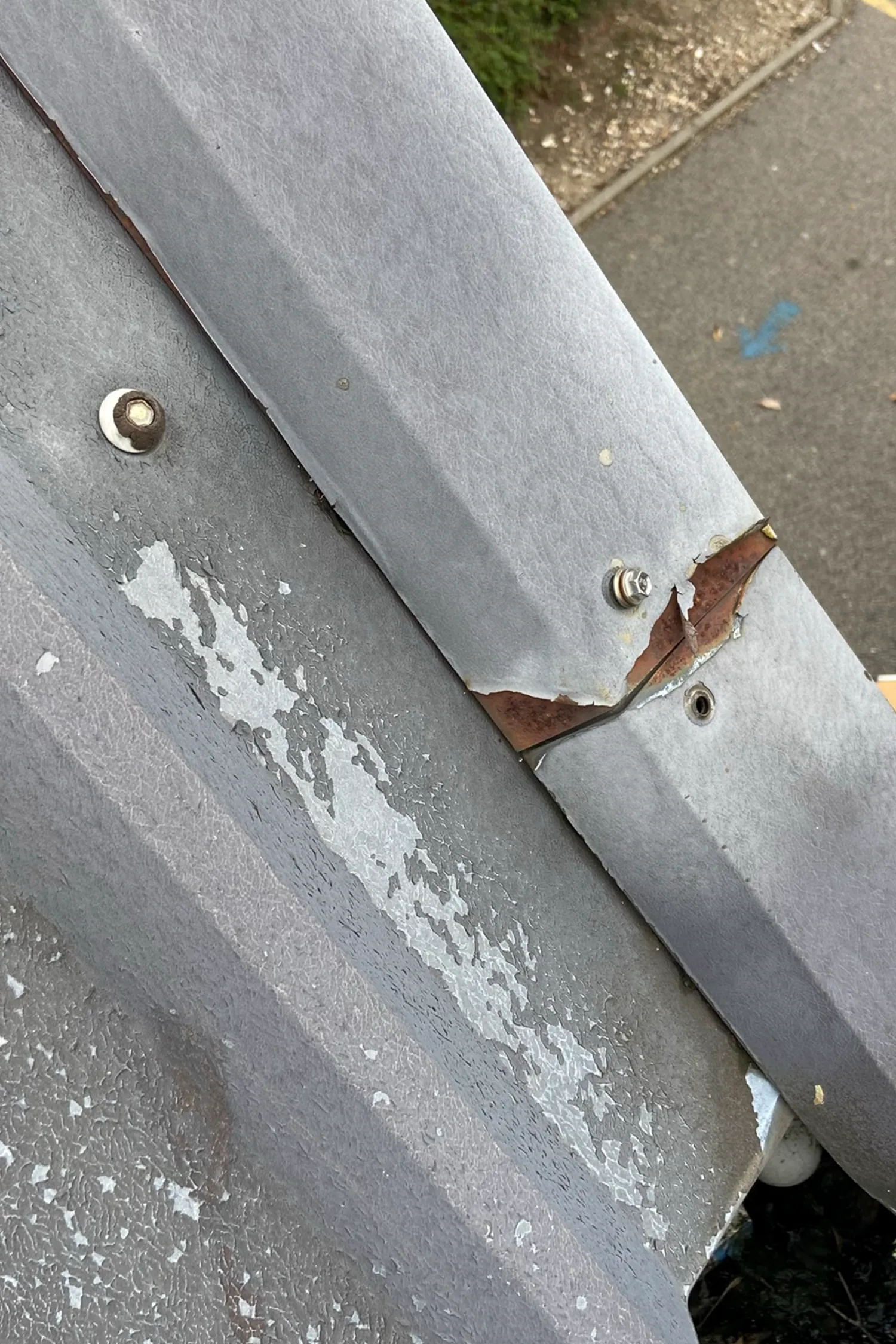Damaged metal roof cladding with rust stains and peeling paint sections