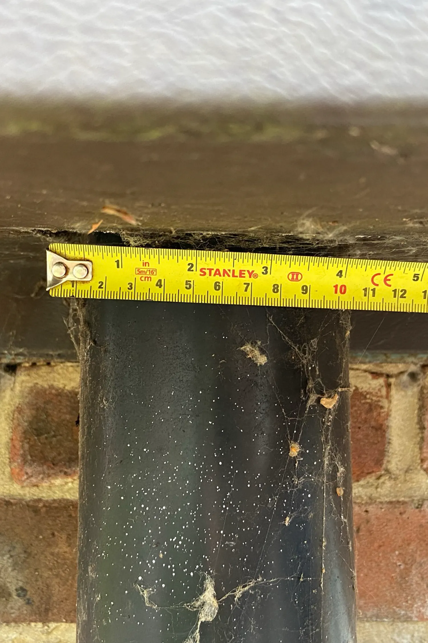 Stanley tape measure against deteriorating dark metal cladding with brick background