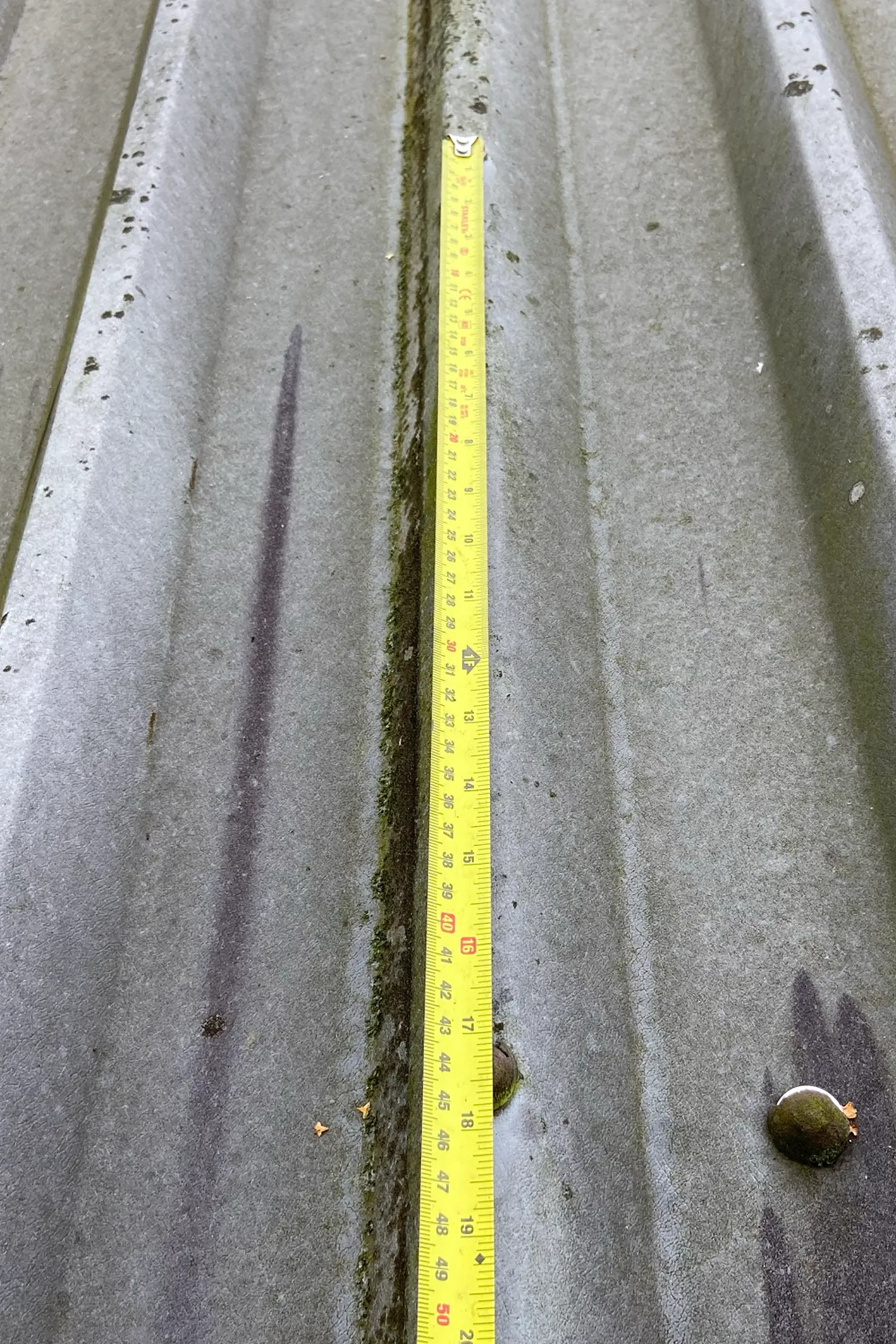 Yellow measuring tape on concrete roof cladding with moss growth
