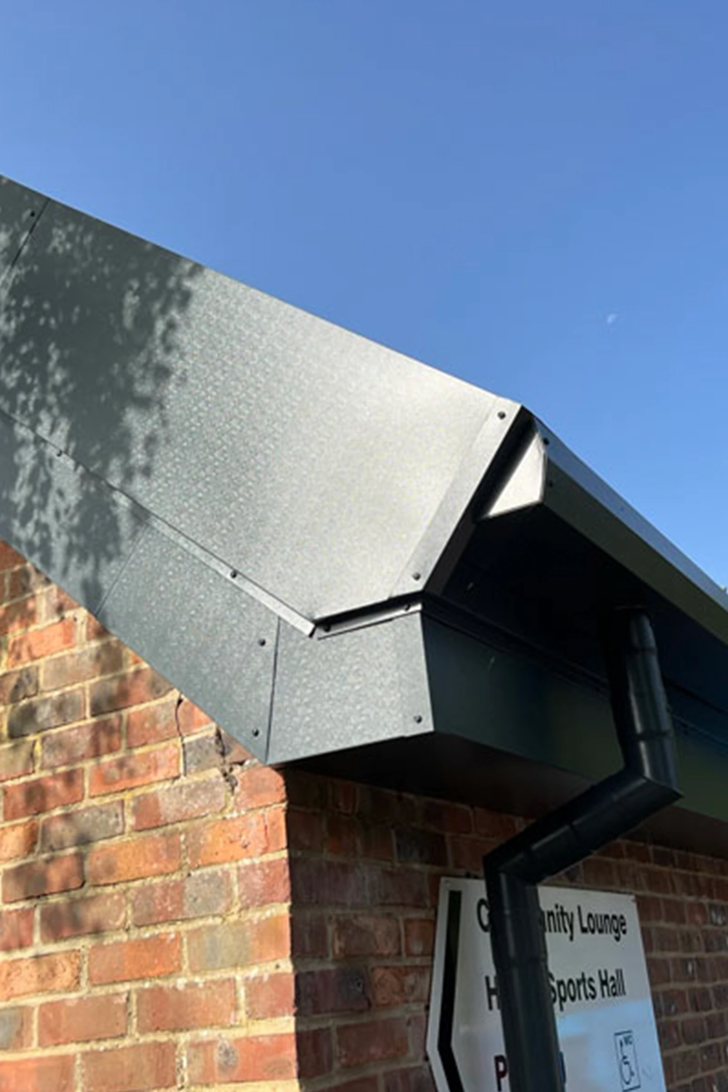 Metal cladding installation on brick building exterior under clear sky