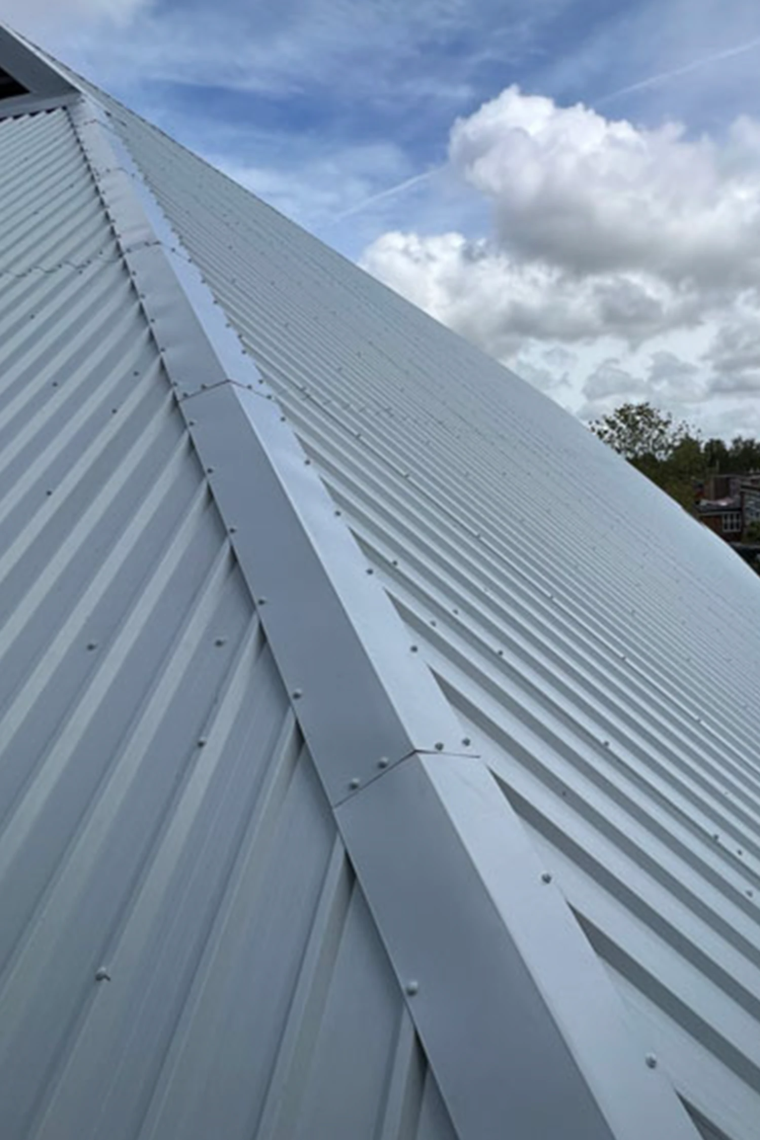 Metal corrugated roof panels with ridge cap and fasteners against cloudy sky