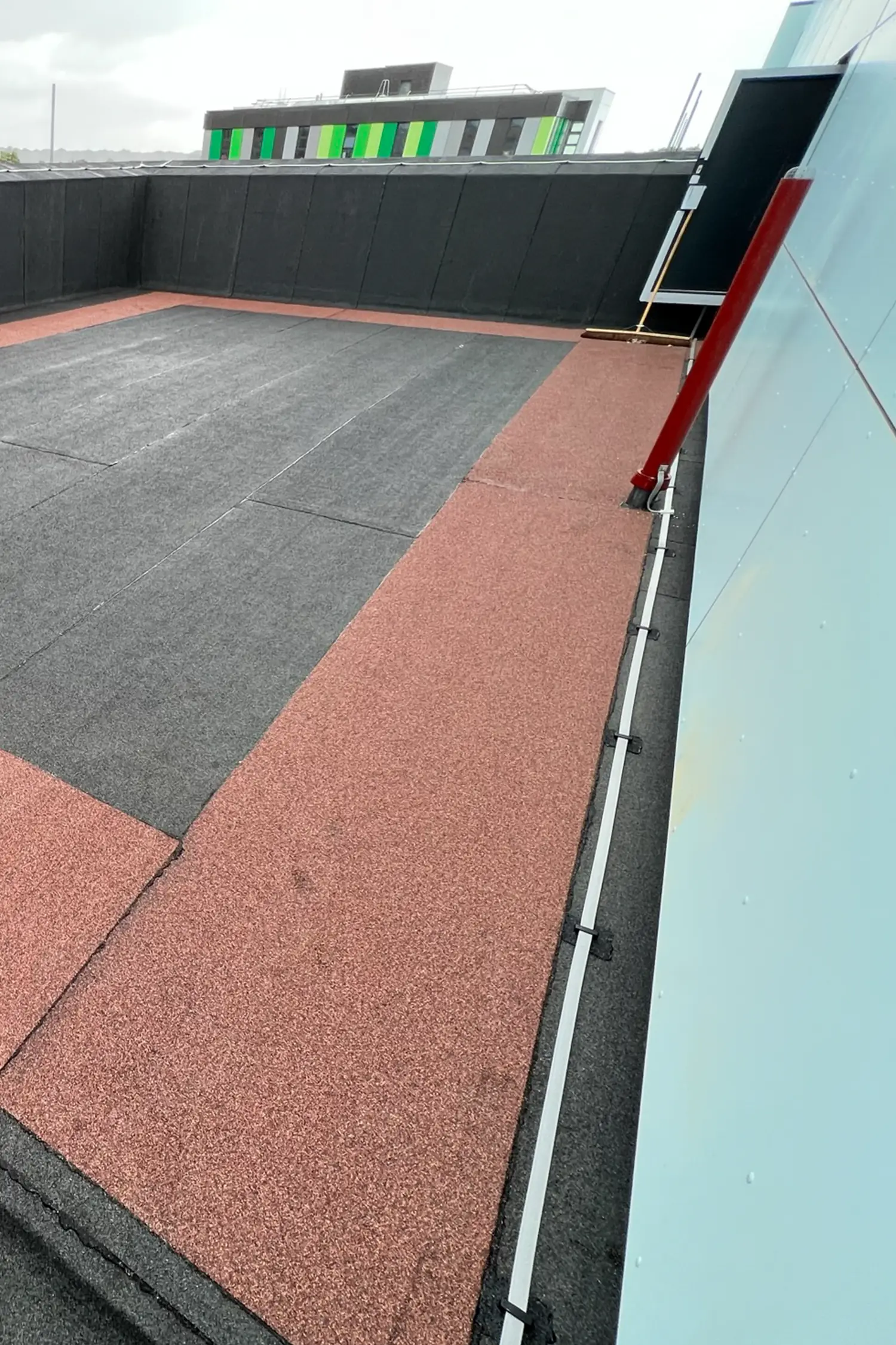 Rooftop terrace with red and gray rubber tiles bordered by black safety railing