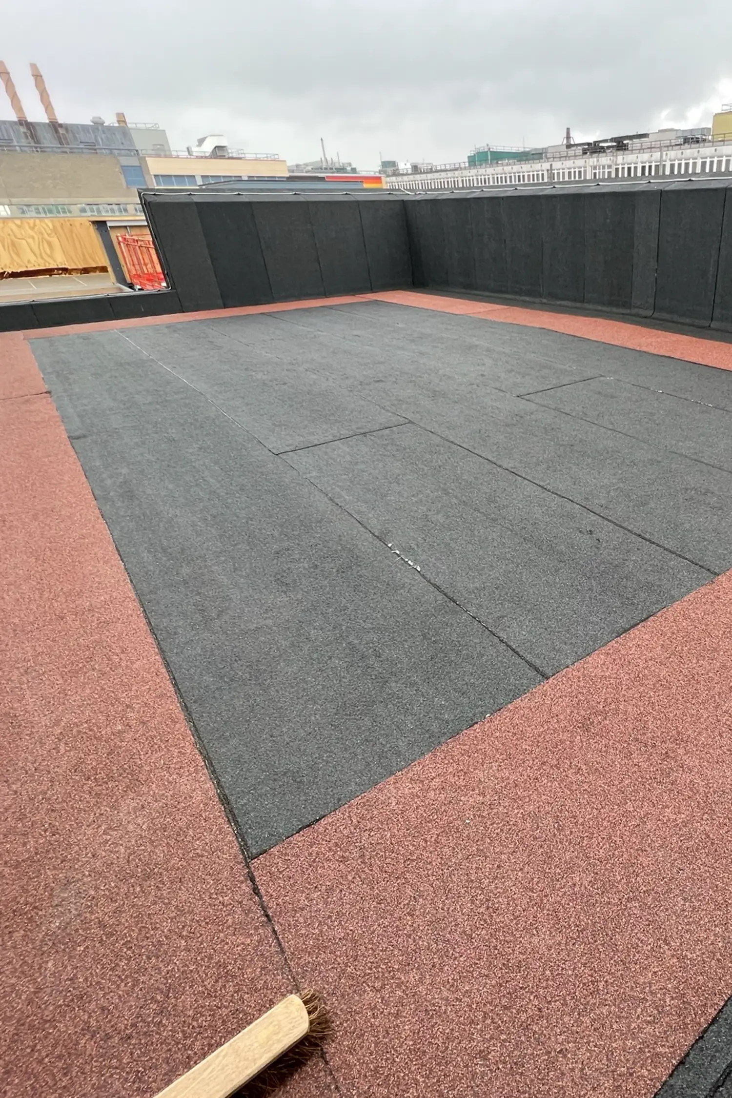 Rooftop terrace with dark gray rubber tiles and red-brown rubber border surface