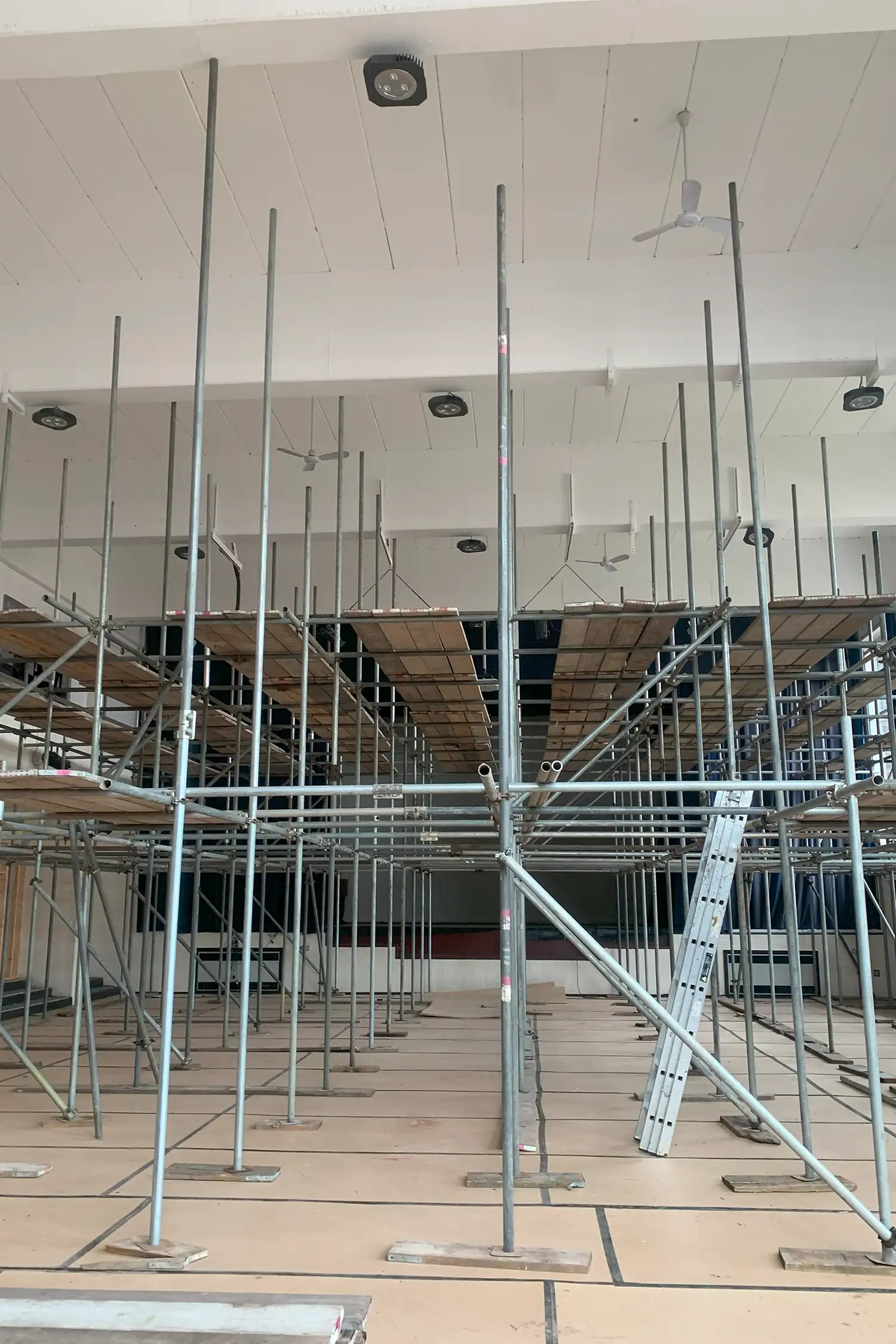 Interior construction site with metal scaffolding and wooden flooring under renovation.