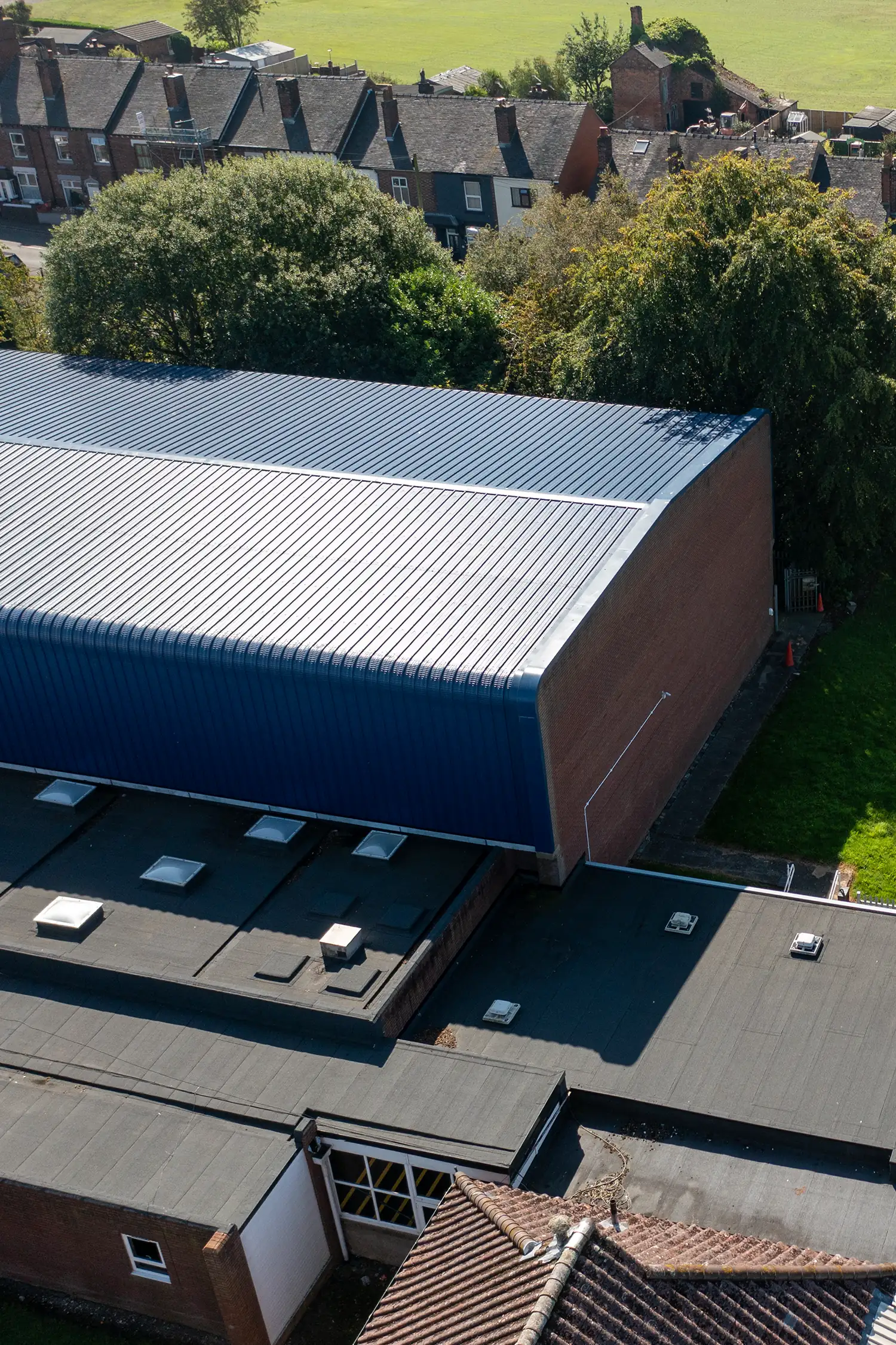Modern corrugated metal roof structure adjacent historic brick buildings and green landscape
