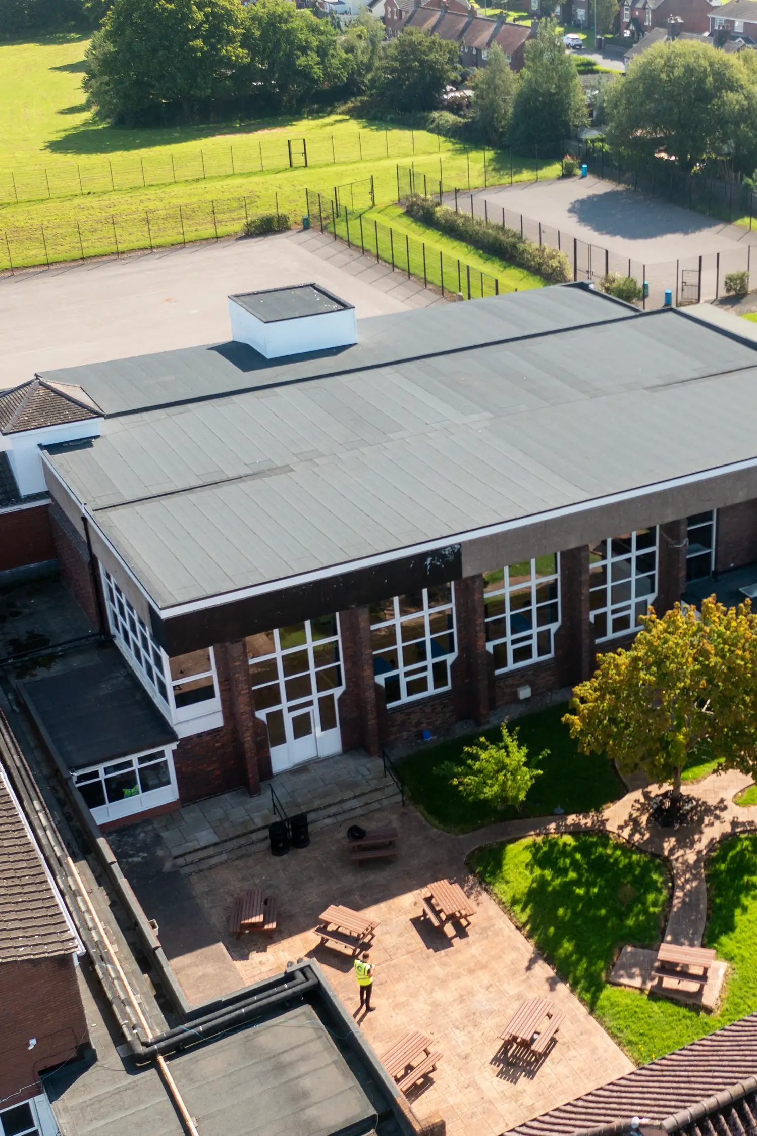 Aerial view of modern school building with flat roof and courtyard area surrounded by fields.
