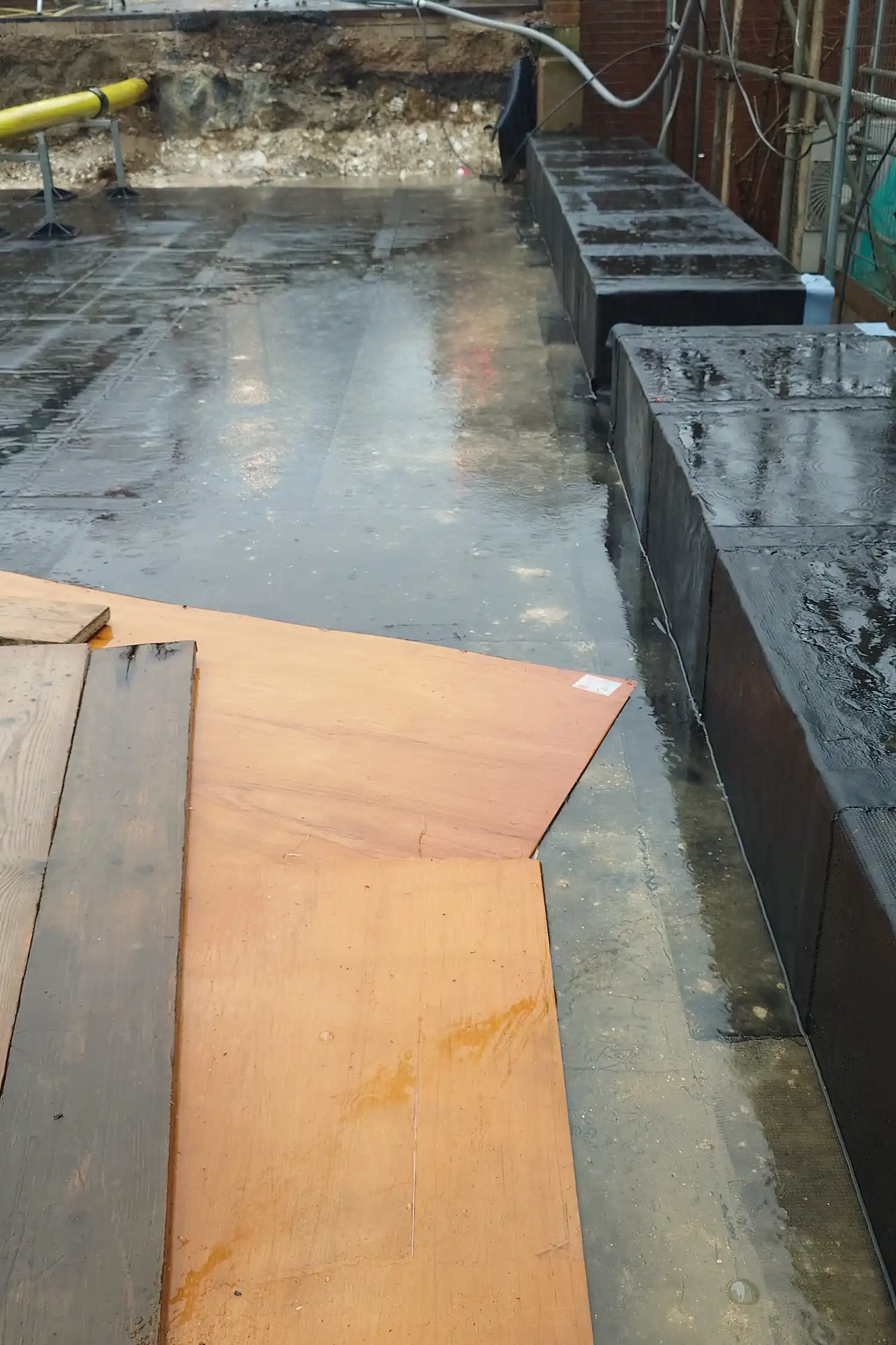 Wet construction site with orange plywood and black drainage containers
