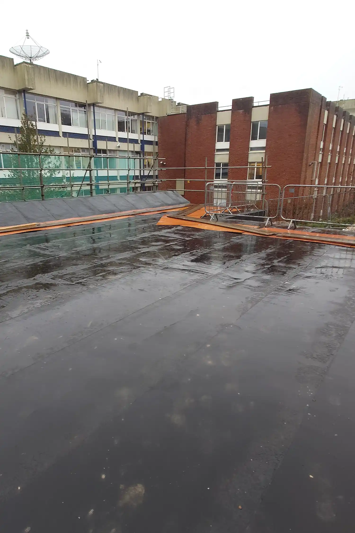 Wet rooftop construction site with orange safety barriers and brick buildings