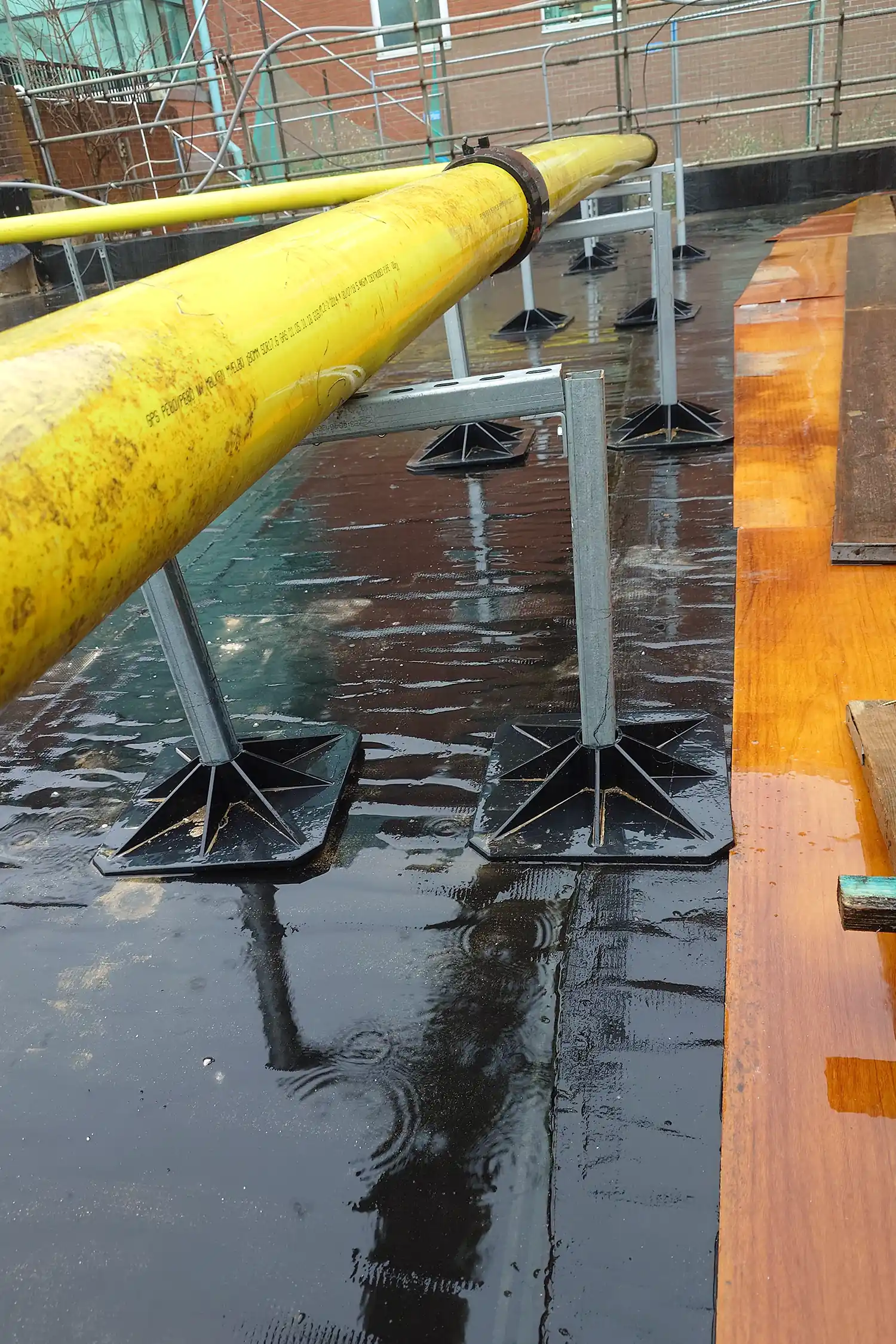 Yellow pipe and support structures on wet green roof surface with scaffolding