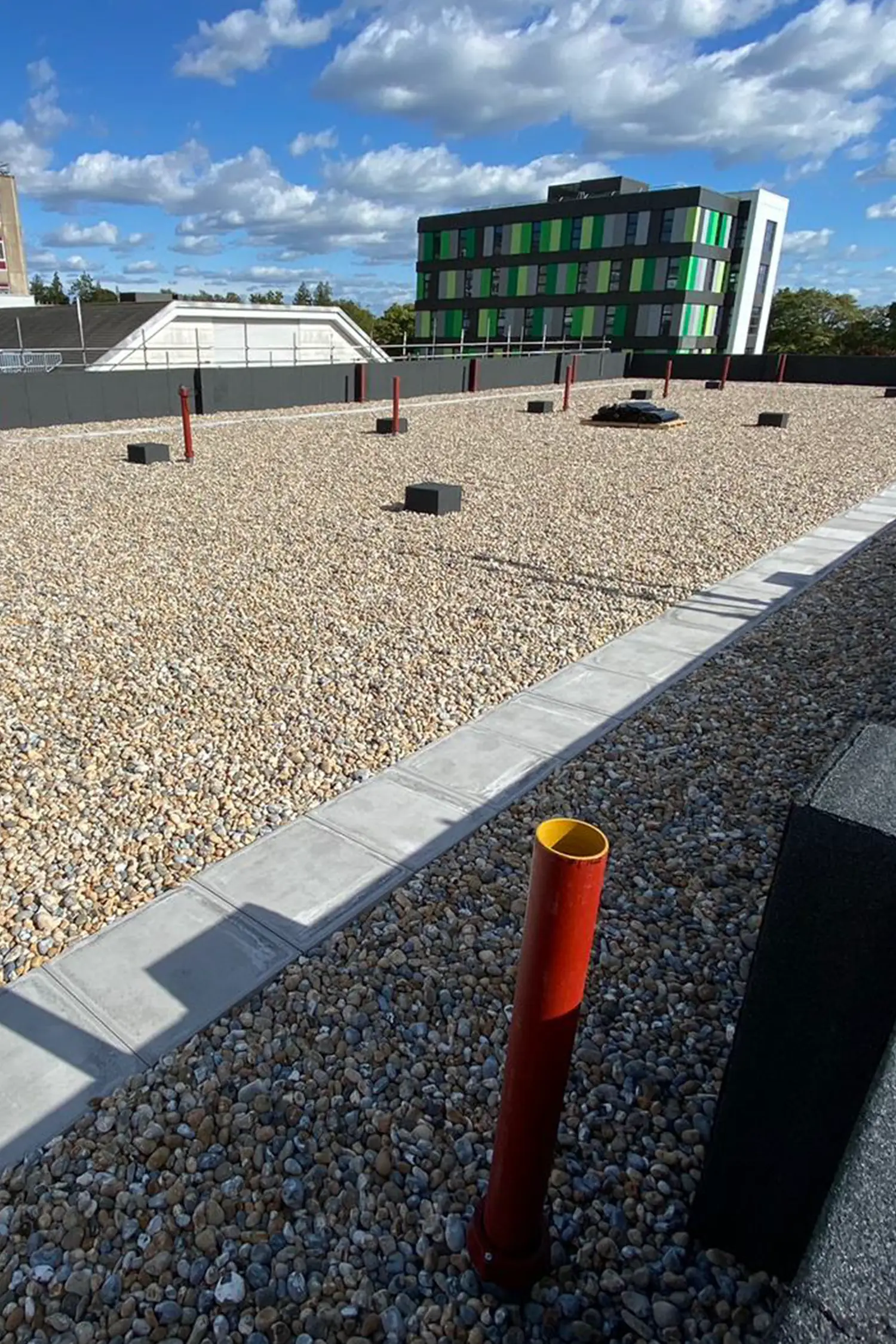 Modern green and black oncology building overlooking gravel courtyard with red bollards