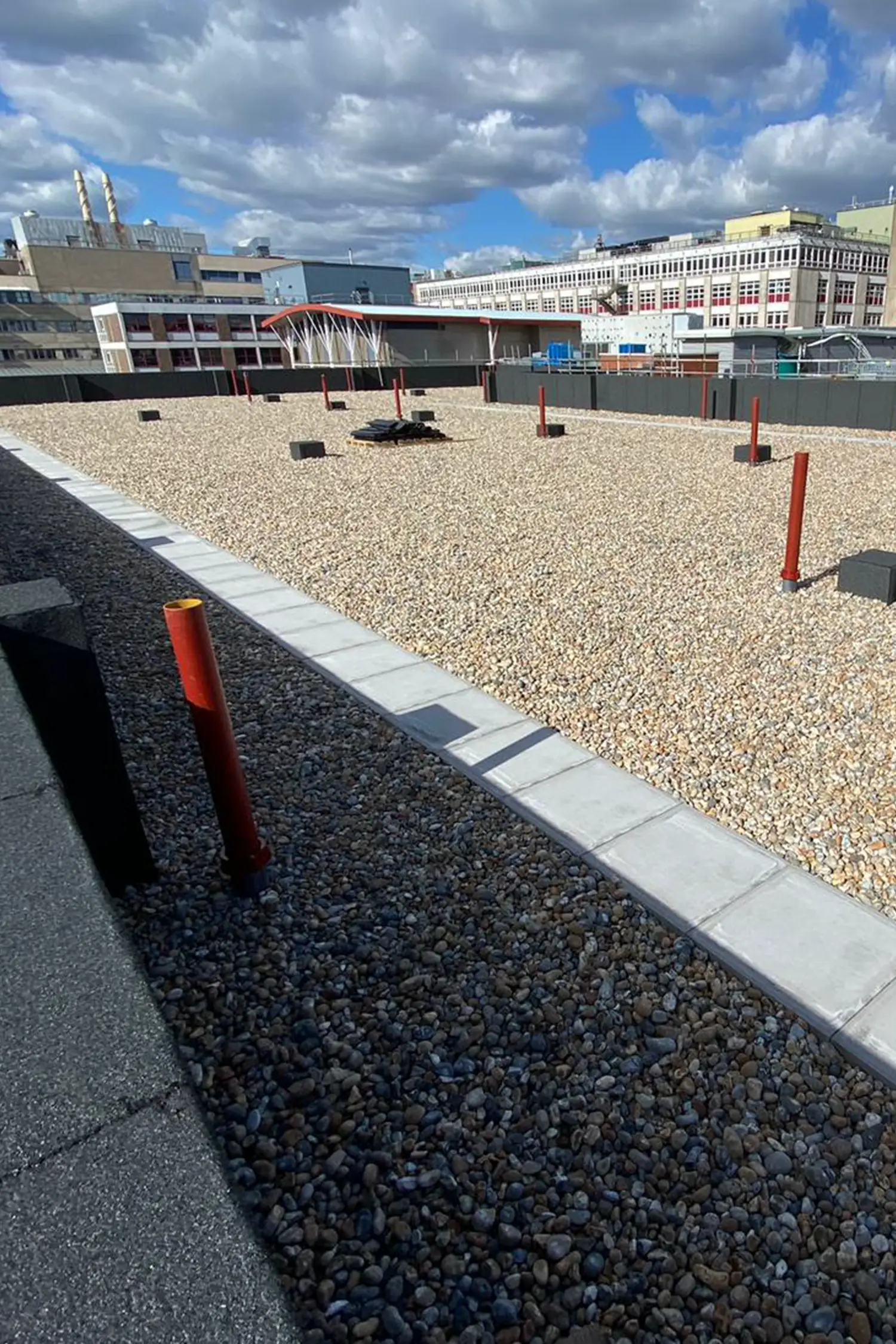 Rooftop gravel area with red bollards and concrete pathways at hospital facility