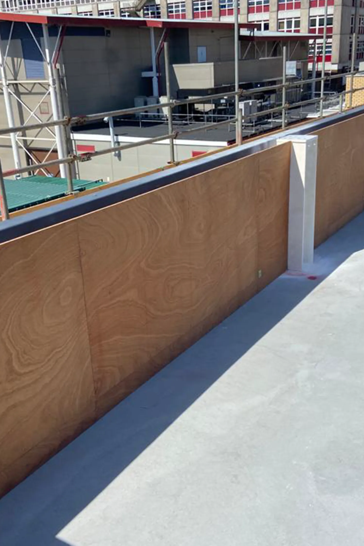 Construction site with wooden barrier wall and metal railings overlooking hospital building