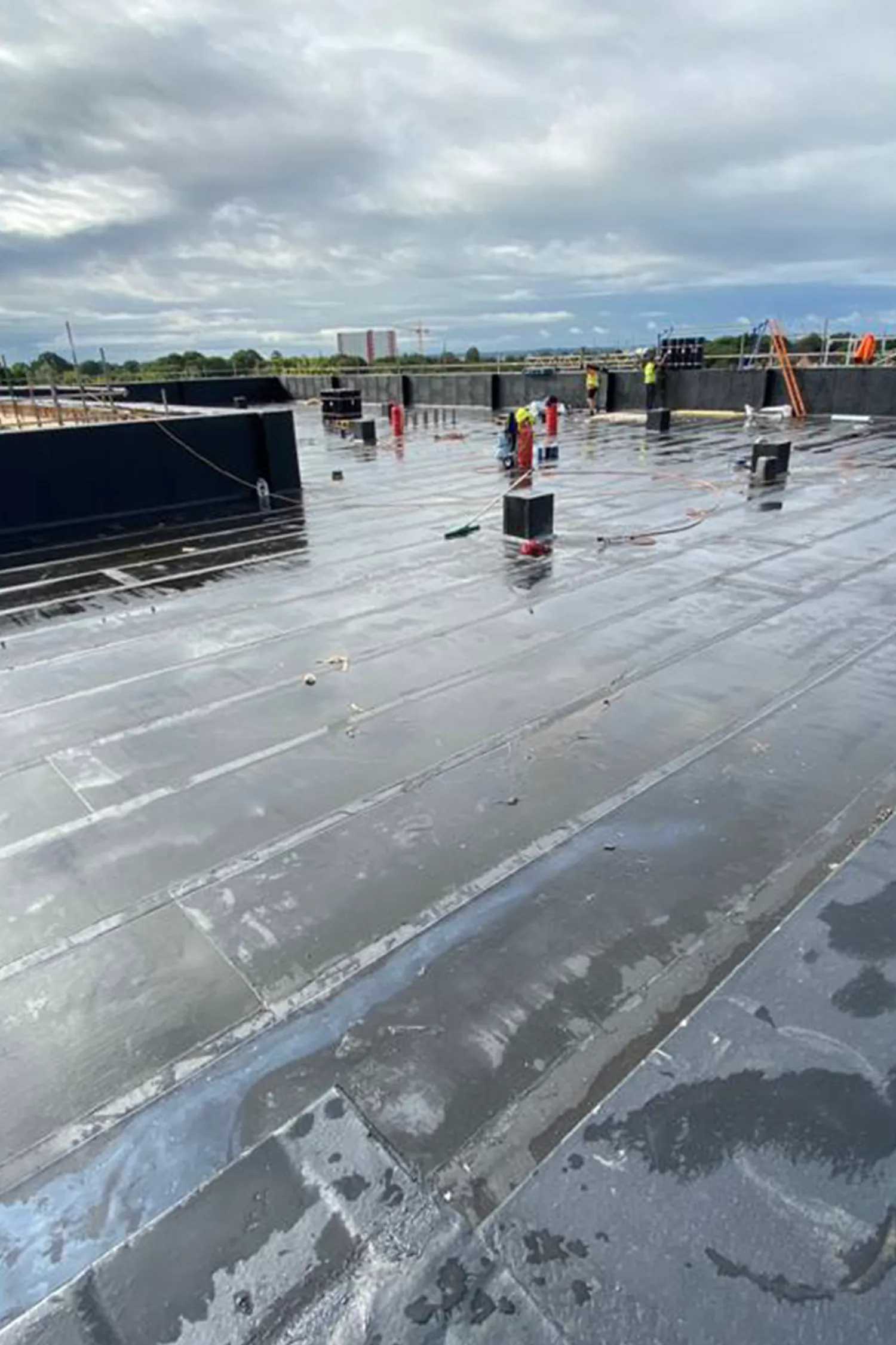 Wet rooftop construction site with workers and safety equipment during daytime