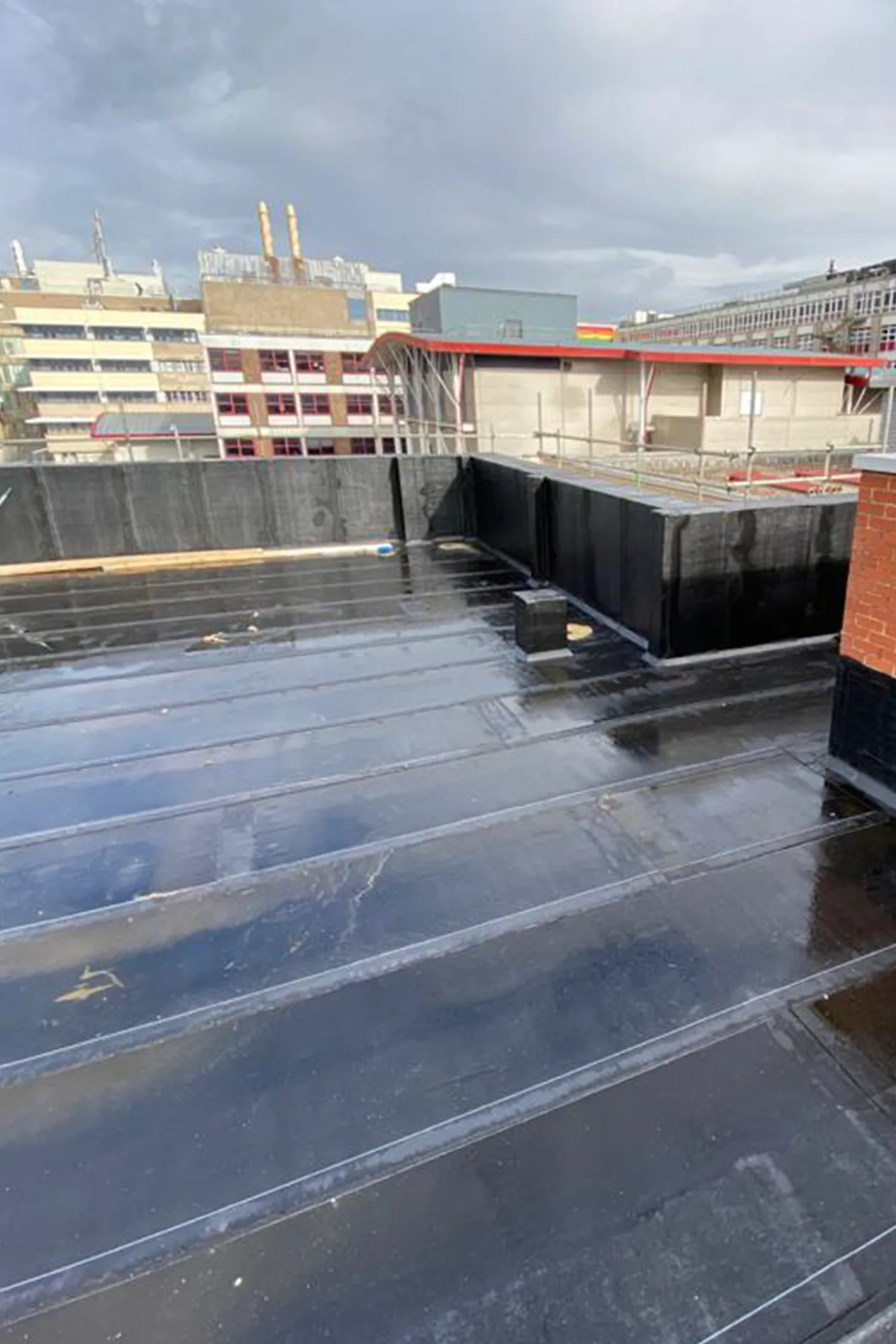 Wet rooftop with black waterproofing membrane and metal structures at hospital facility