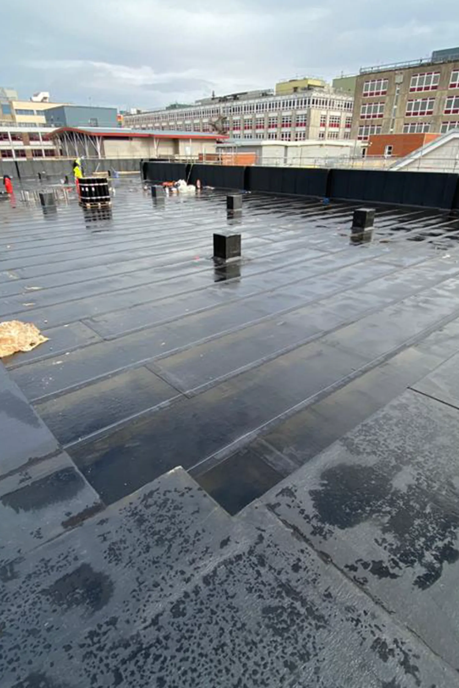 Wet rooftop construction site with black membrane and metal posts during installation