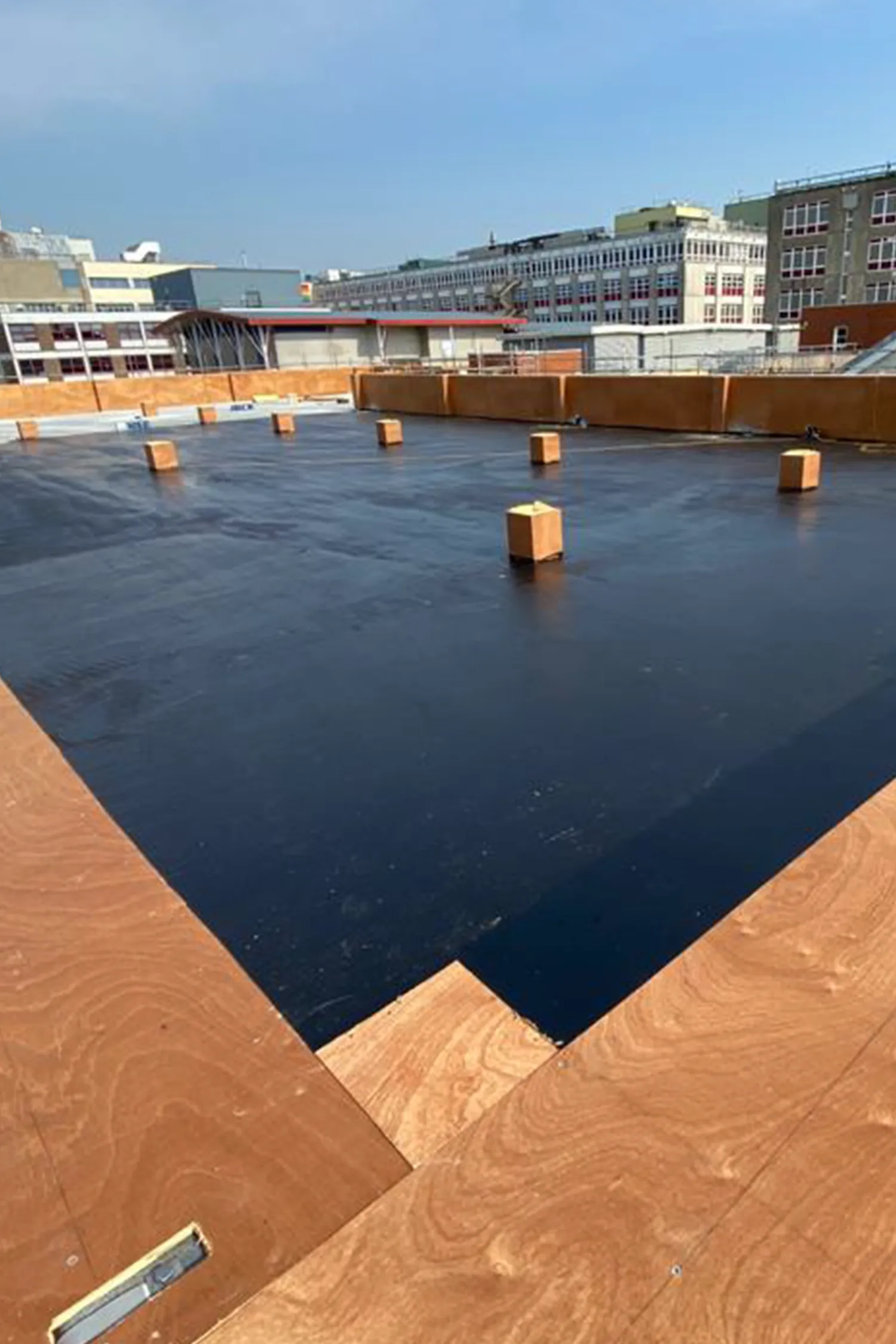 Rooftop construction site with dark waterproofing membrane and orange brick barriers