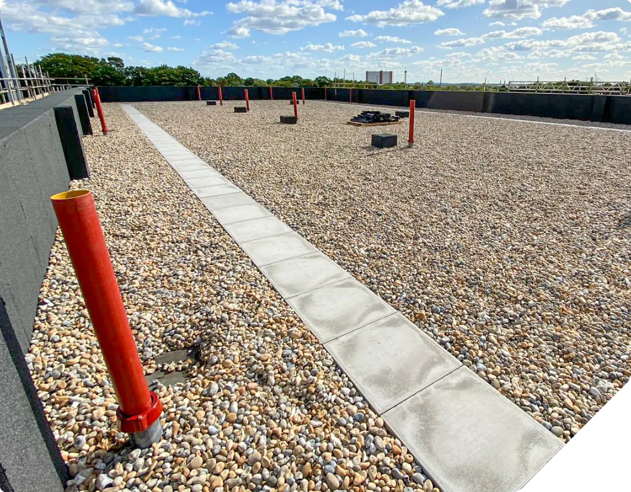 Rooftop terrace with gravel, paving stones, red bollards, and industrial skyline view.
